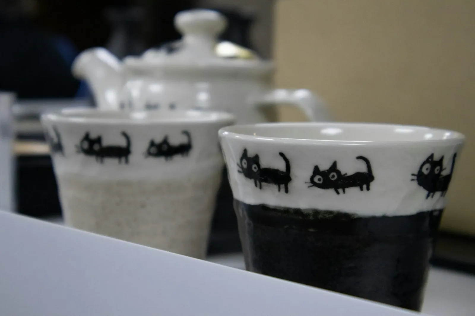 Two ceramic cups with black cat illustrations around the rim on a shop counter
