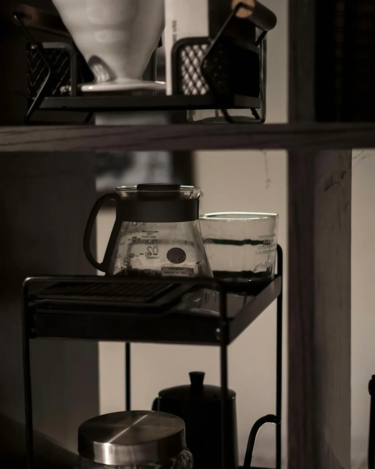 Black metal utility cart with a pour-over dripper and glass carafe on top and a kettle and canister on the lower shelves