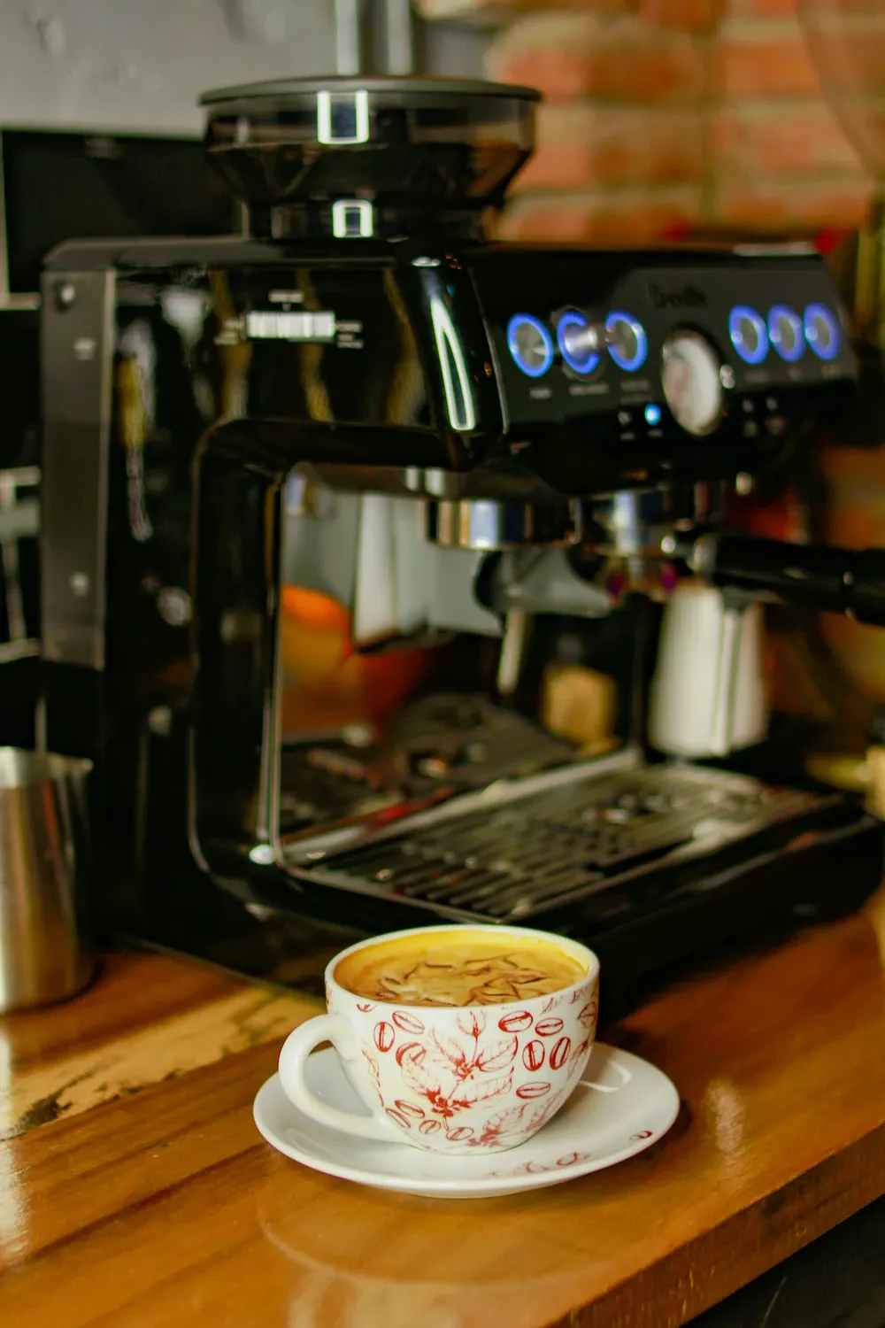 Black Breville espresso machine with a built-in grinder and a latte in a patterned cup on a wood counter