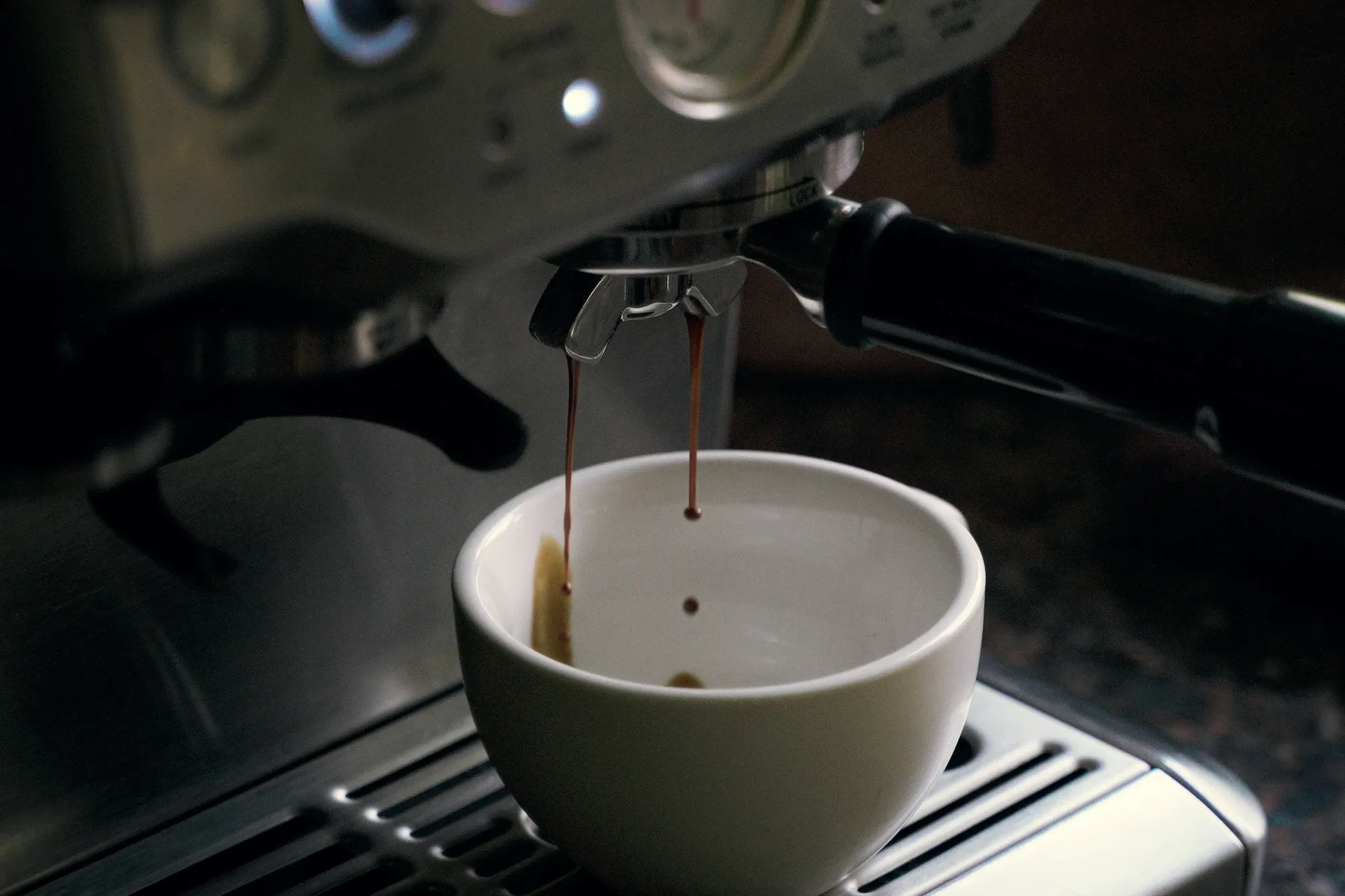 Brushed stainless Breville espresso machine brewing into a gray ceramic cup on the drip tray