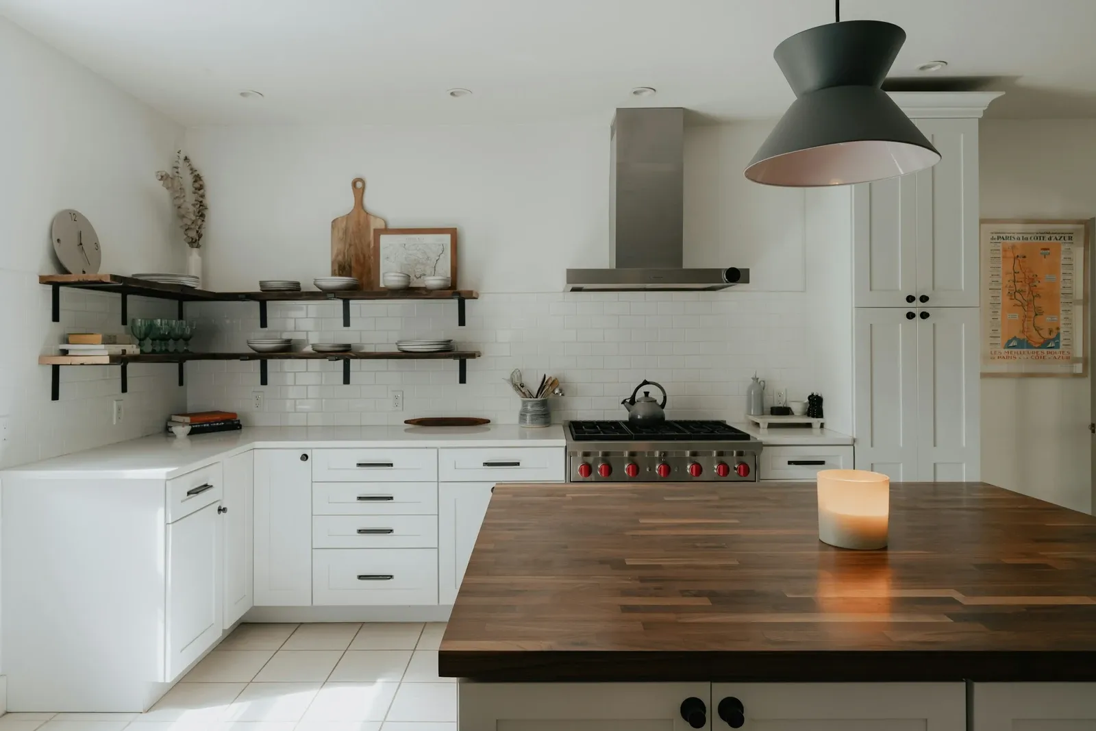 Kitchen island with a thick wood butcher block counter, white cabinets and pendant lights over a range
