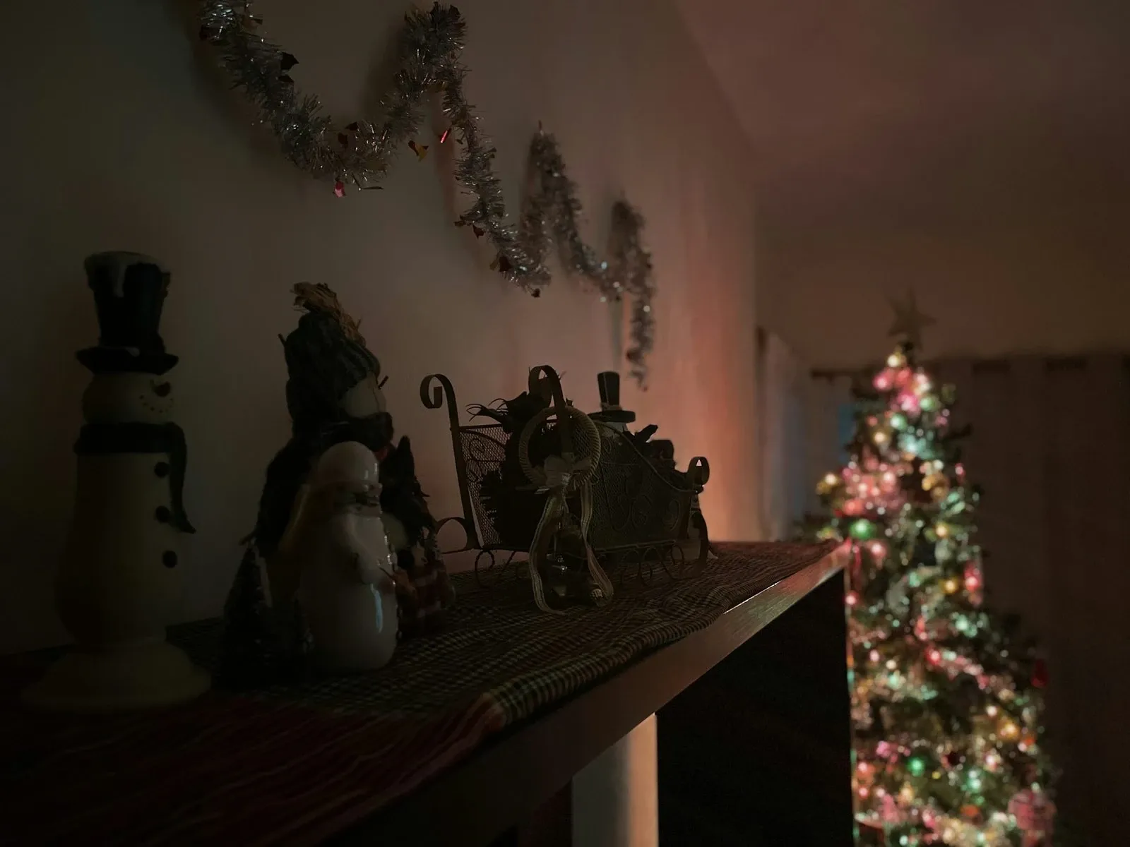 Shelf with snowman figurines, a small lit Christmas tree and candles in a dim room