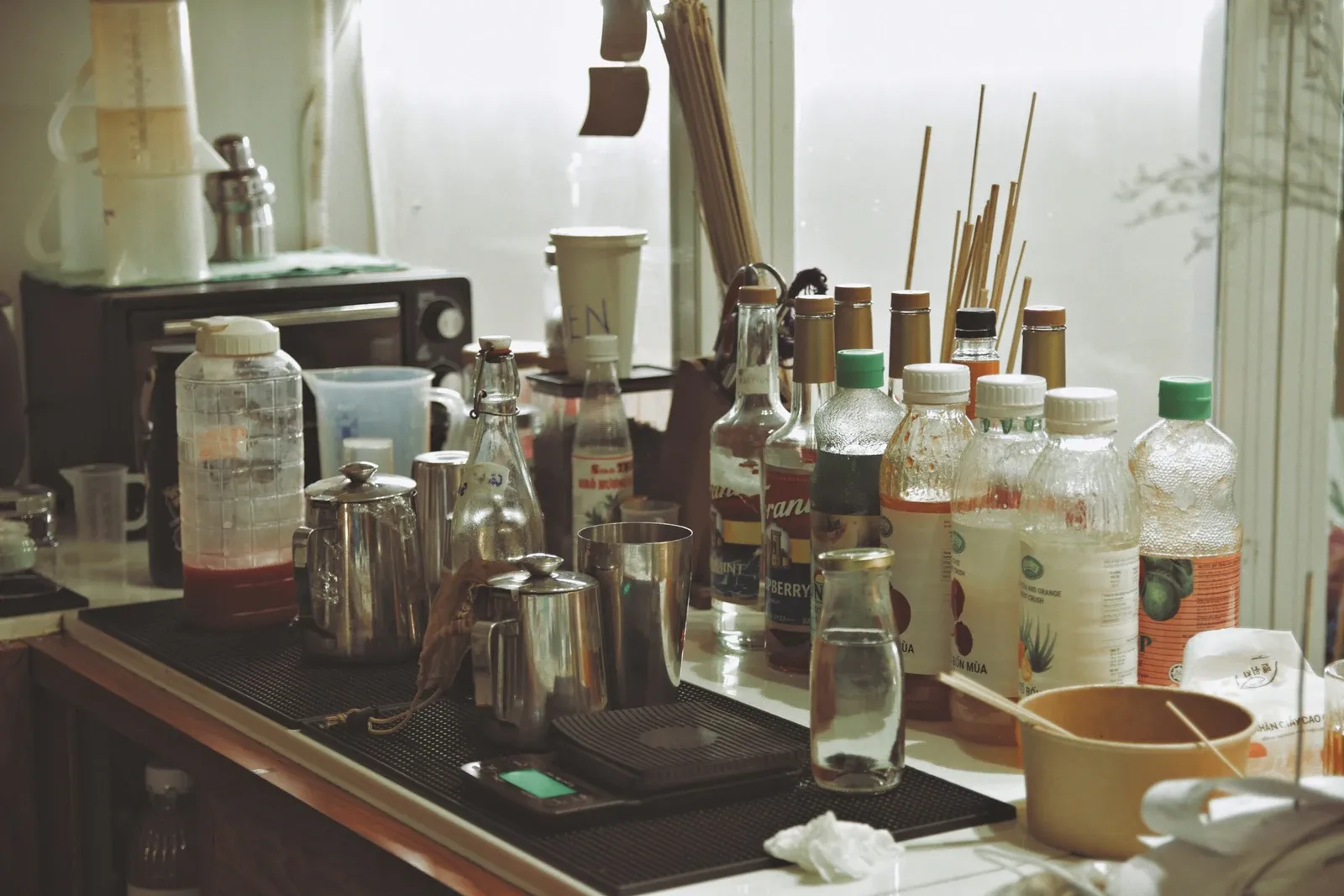 Kitchen counter crowded with bottles, jars, kettles and utensils with no clear zone for making coffee