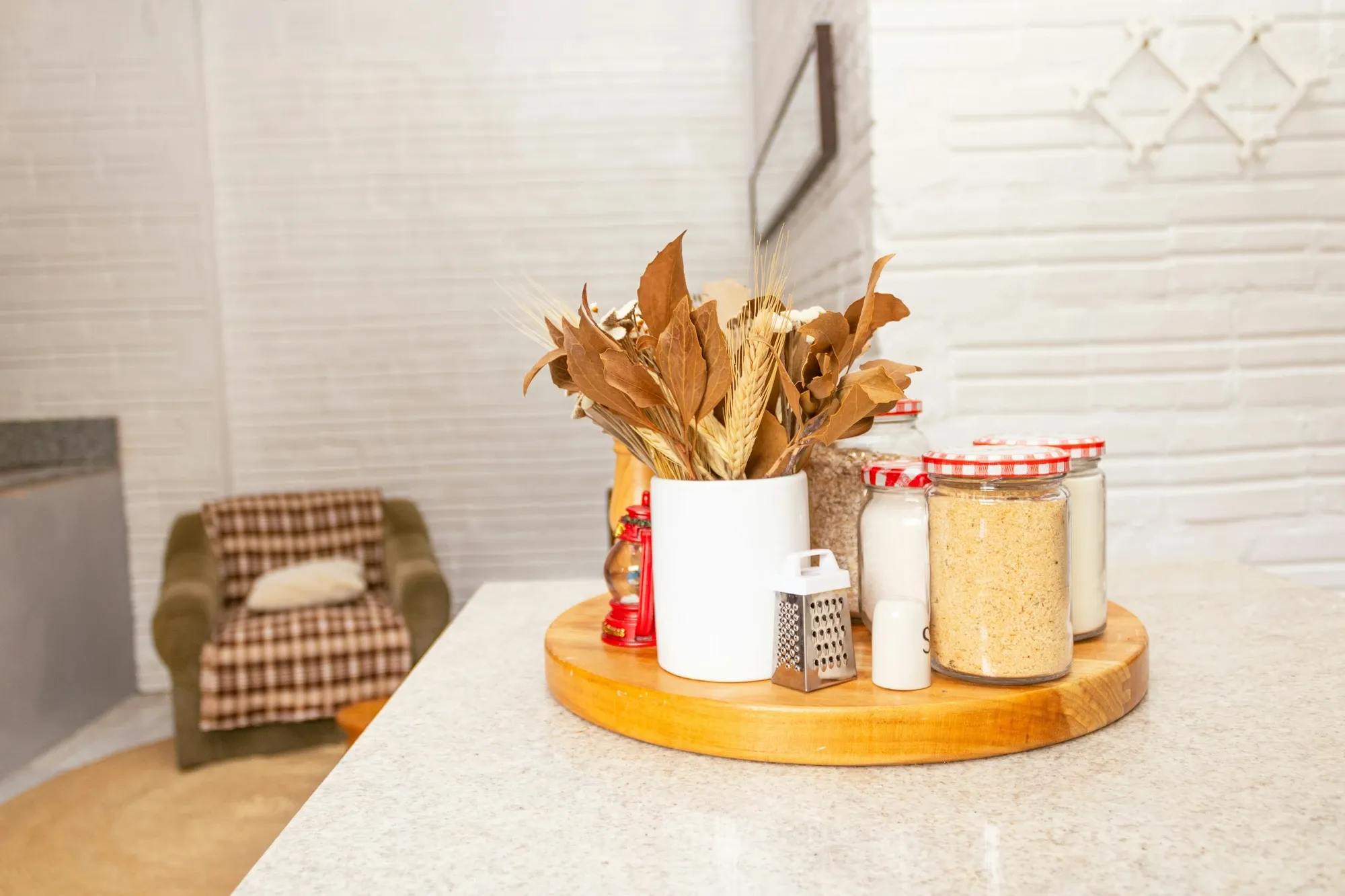 Round wood turntable on a kitchen island with glass jars, a white pitcher of dried flowers and a grater