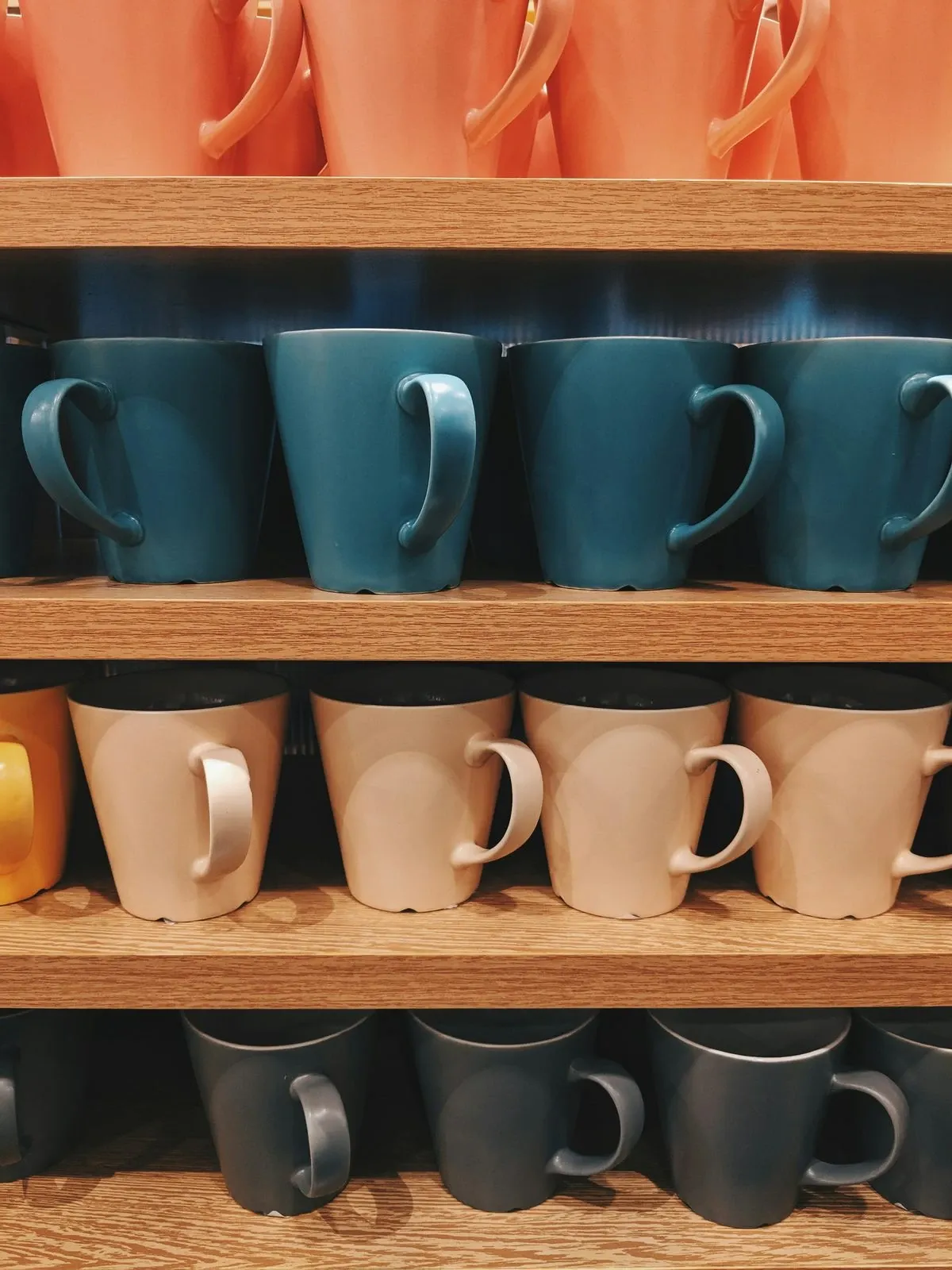 Wood shelves stacked with matching mugs in teal, blush, coral and black