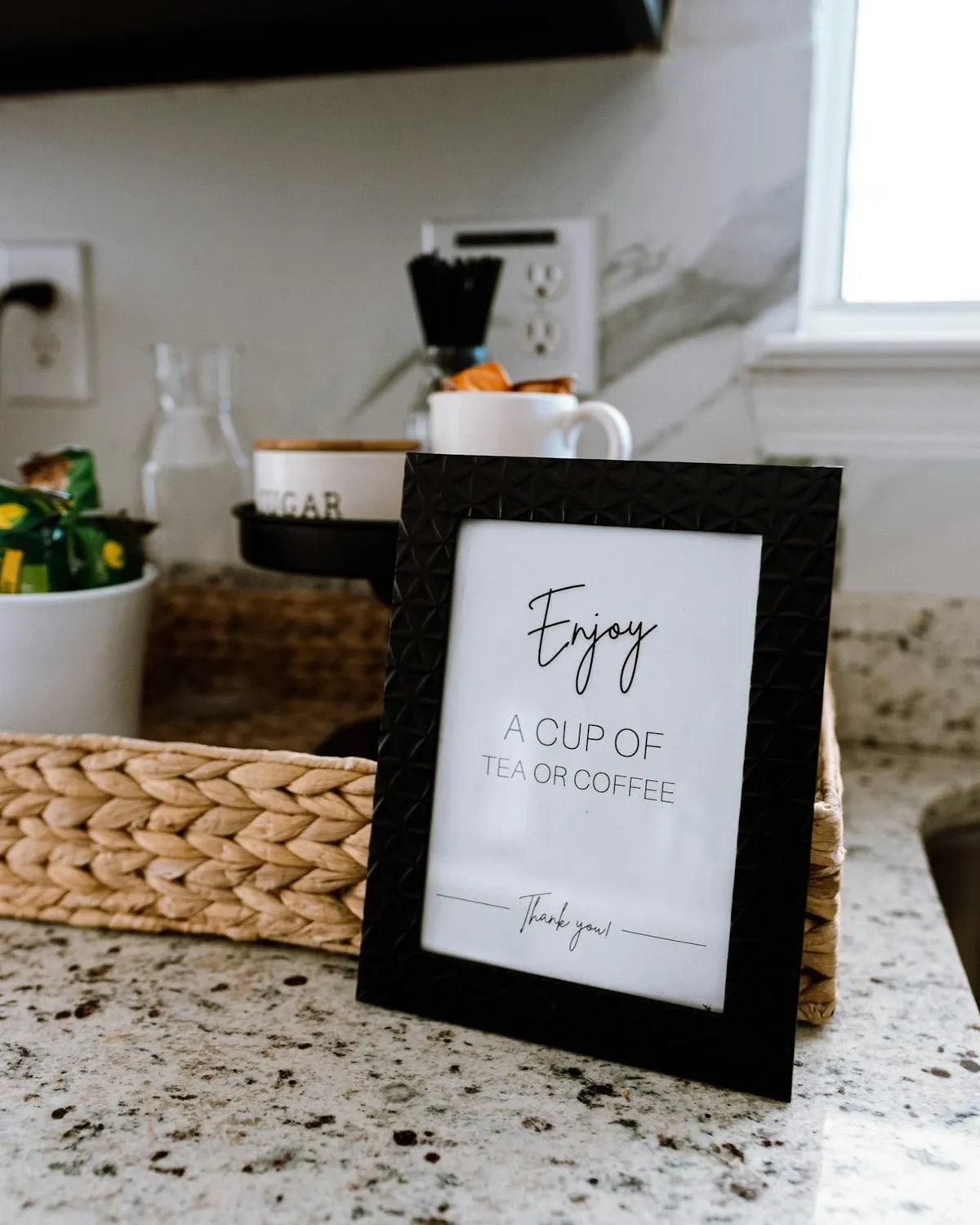 Framed print leaning on a kitchen counter tray beside a small plant and kitchen items