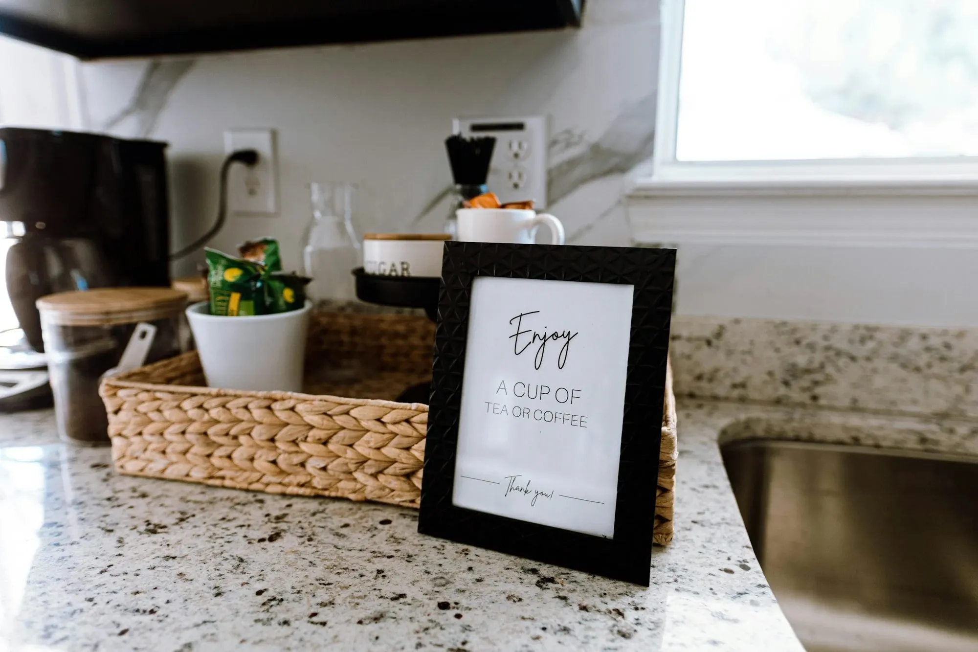 Framed sign leaning on a kitchen counter next to a tray with coffee supplies