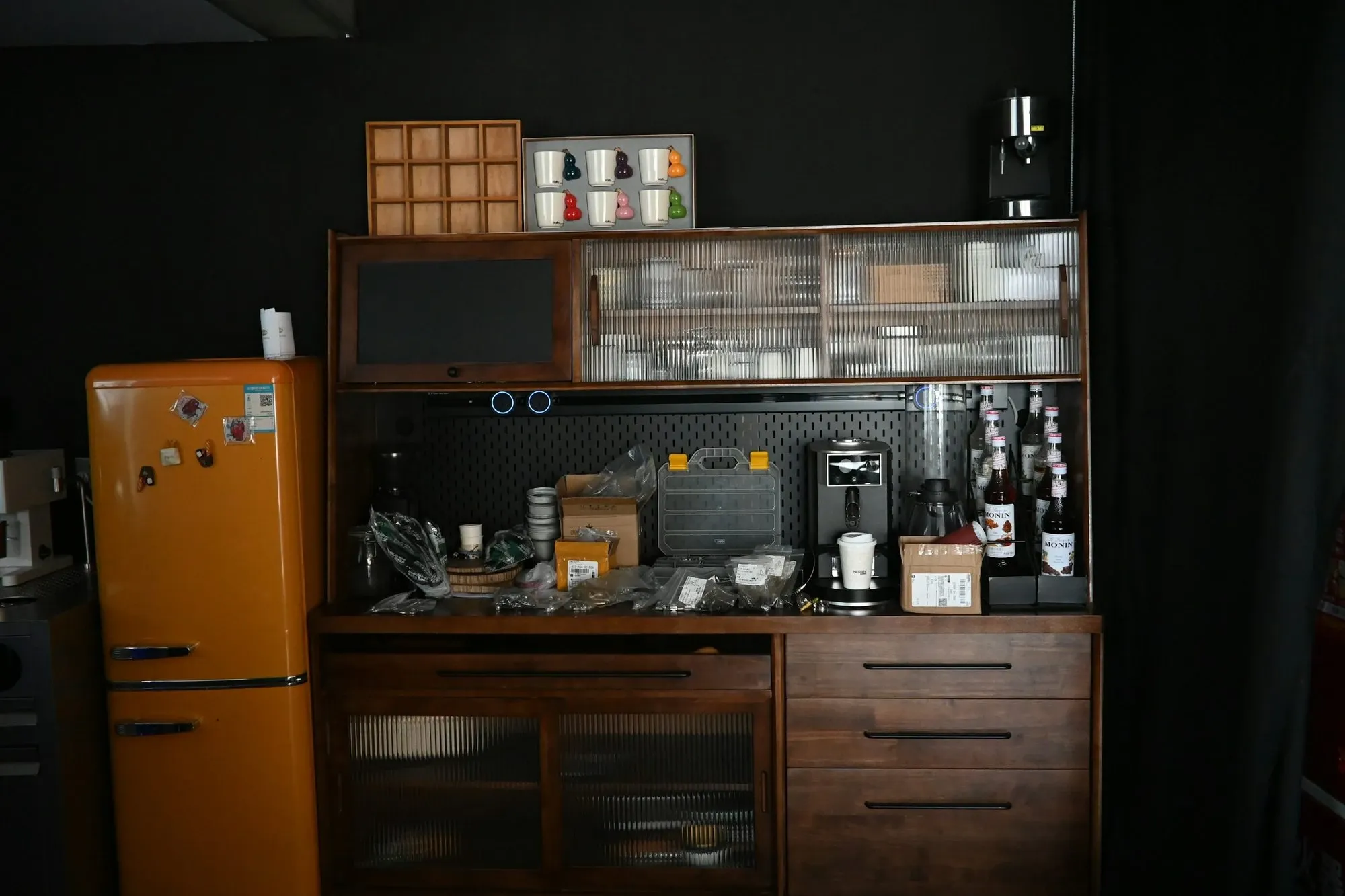 Dark wood cabinet coffee station with open shelves next to a retro orange mini fridge