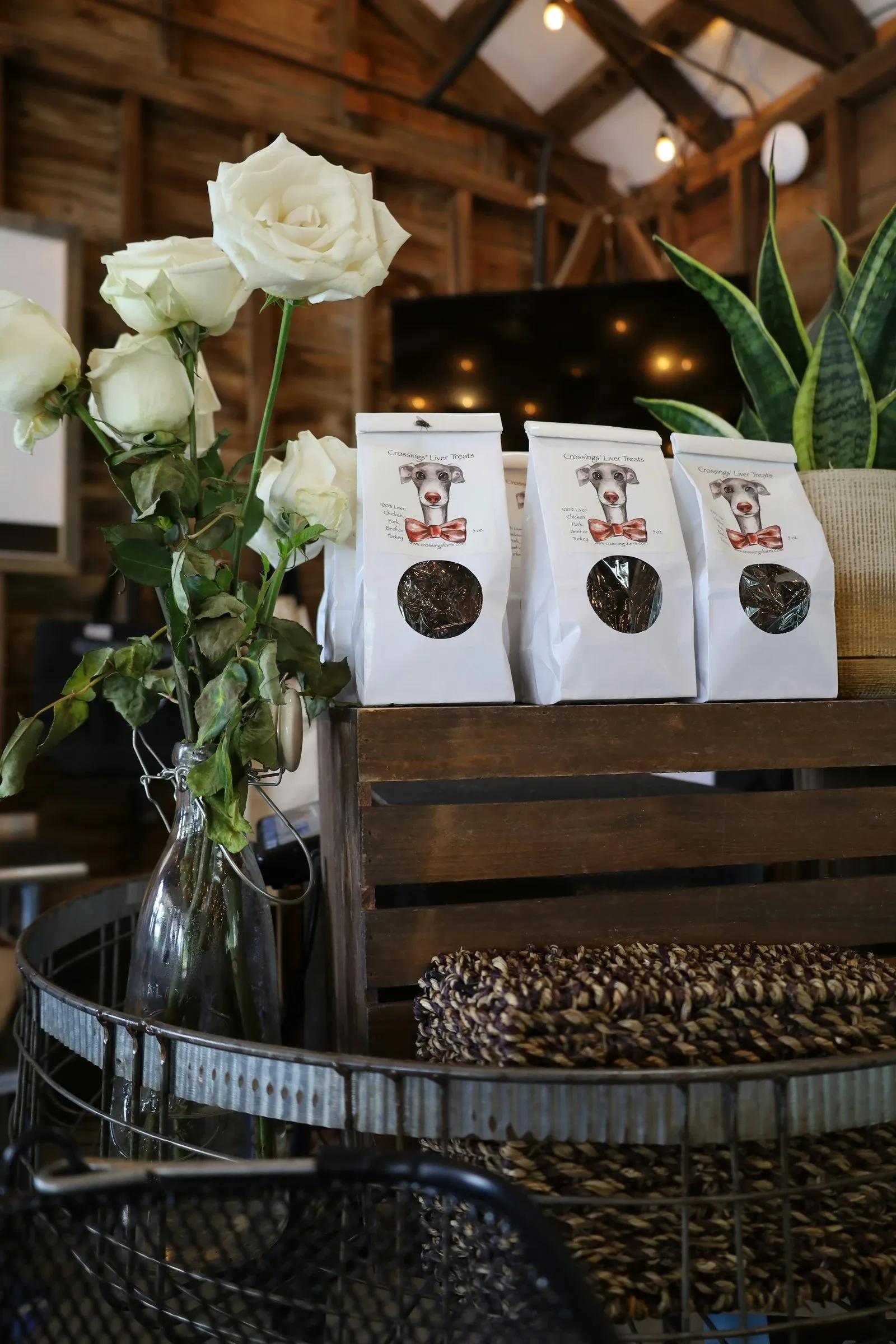 Three white bags of specialty coffee lined up on a wooden counter in a cafe with white roses