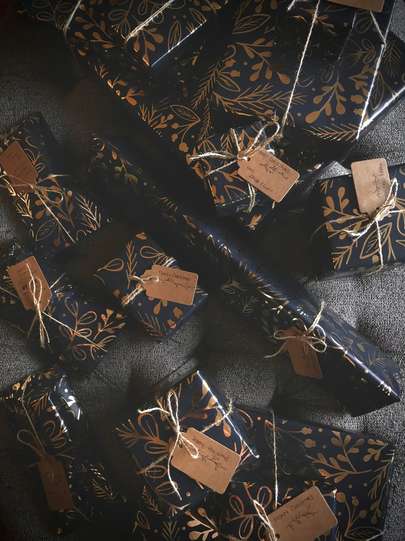Gifts wrapped in dark patterned paper with twine and blank kraft tags laid on a table