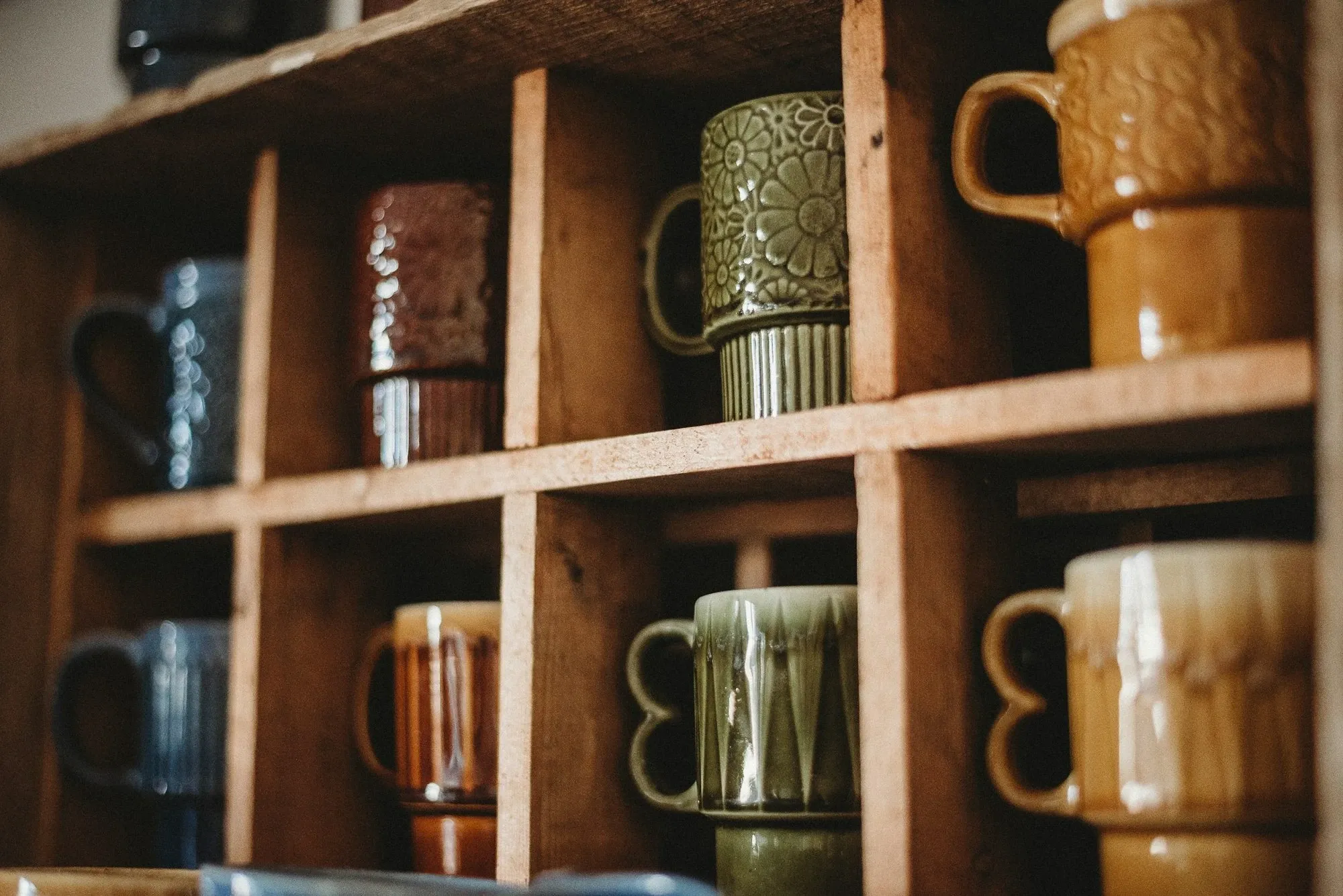 Wooden cubby shelf holding rows of stoneware coffee mugs in warm earthy glazes