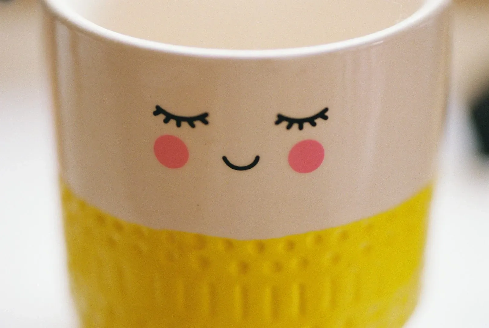 Ceramic mug with a sleepy smiling face and pink cheeks on a pale pink upper half and a yellow textured base