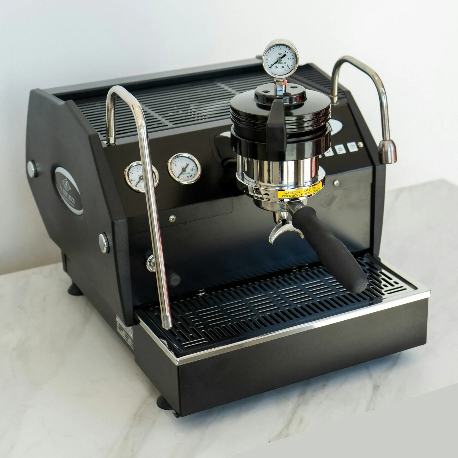 Black prosumer espresso machine with pressure gauges and a chrome group head on a marble counter