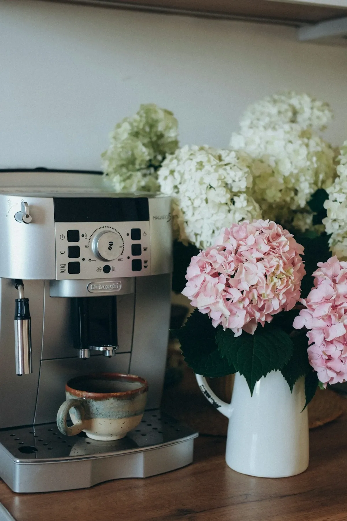Silver bean-to-cup espresso machine beside a vase of pink and white hydrangeas on a counter