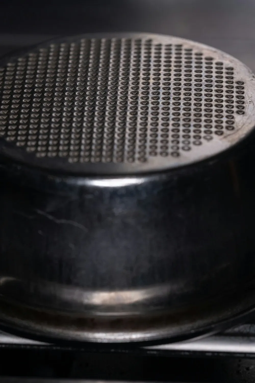 Close-up of a dark espresso filter basket with a perforated metal screen