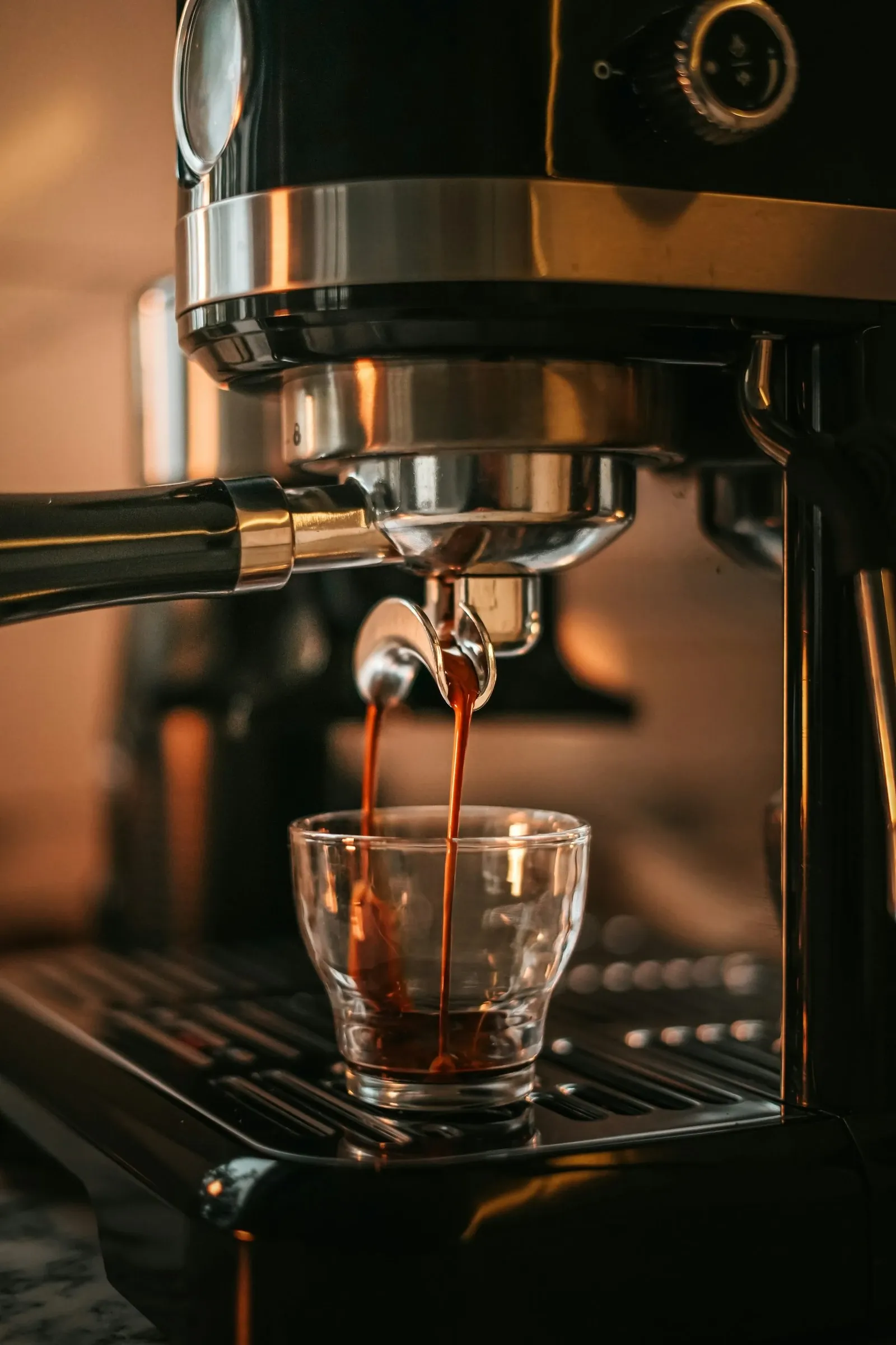 Espresso shot pouring from a machine into a small clear glass cup