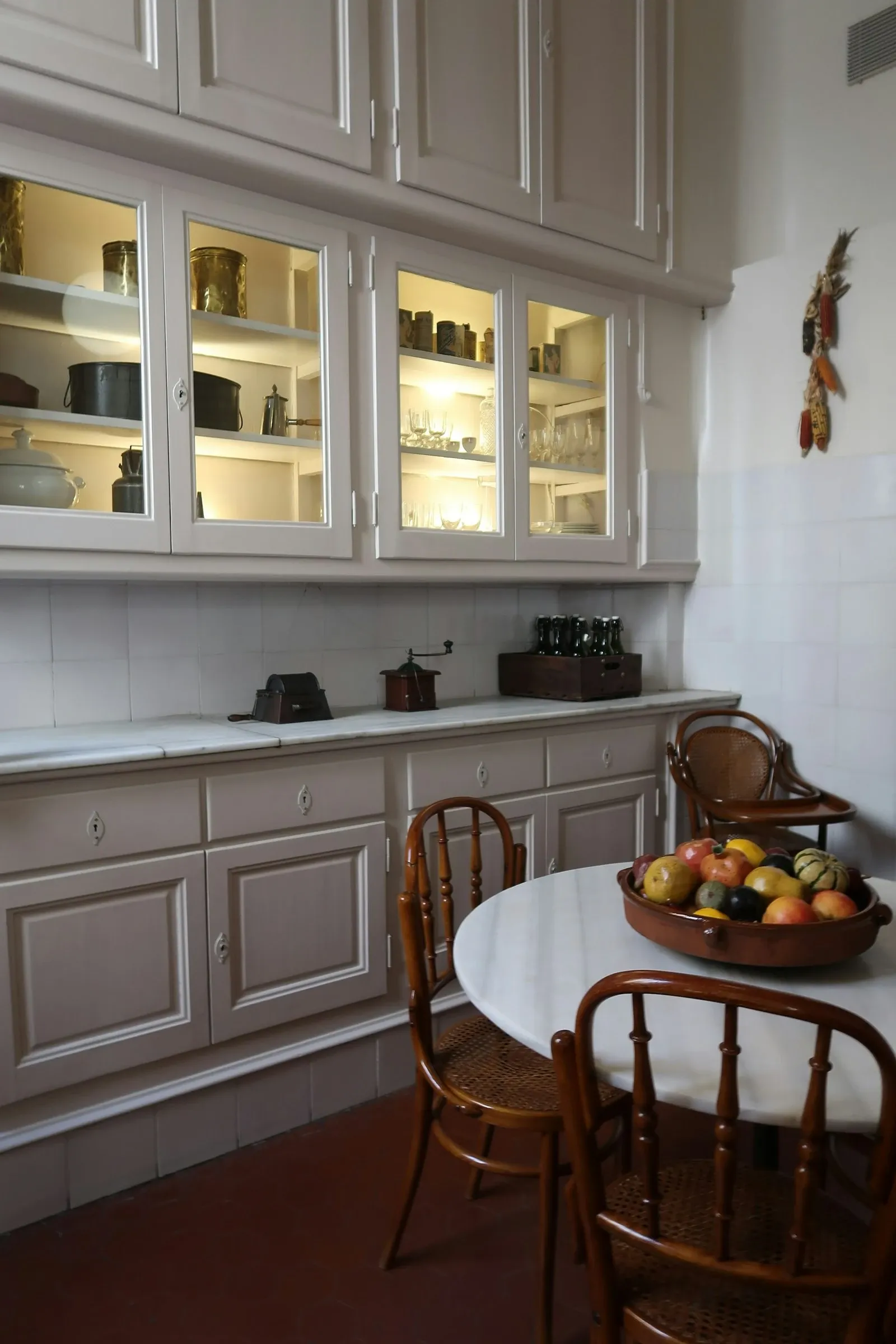 Cream farmhouse kitchen with lit glass-front upper cabinets above a counter and a round wood table