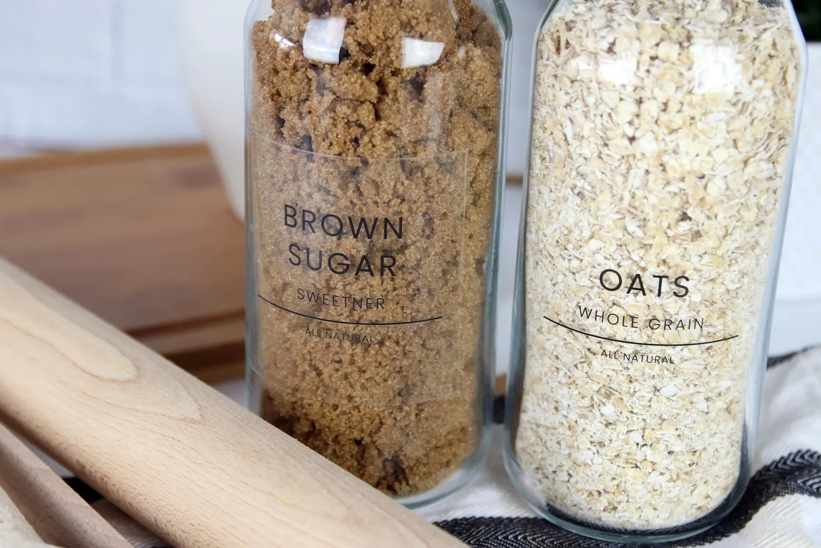 Two tall glass jars of brown sugar and oats with printed sticker labels