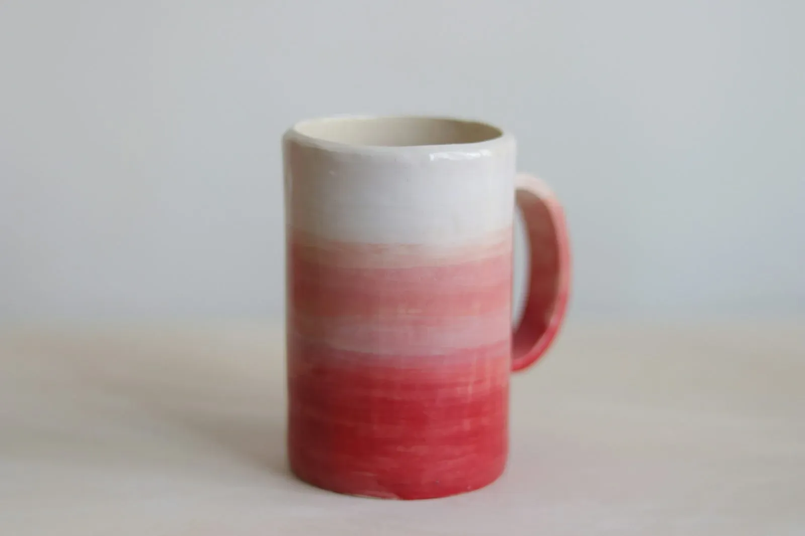 Handmade ceramic mug with a white glaze fading into a pink dip glaze at the base