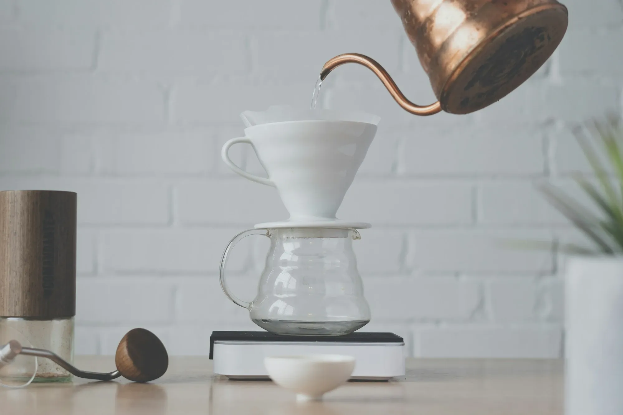 Hand pouring from a gooseneck kettle into a white V60 dripper on a glass server on a white counter