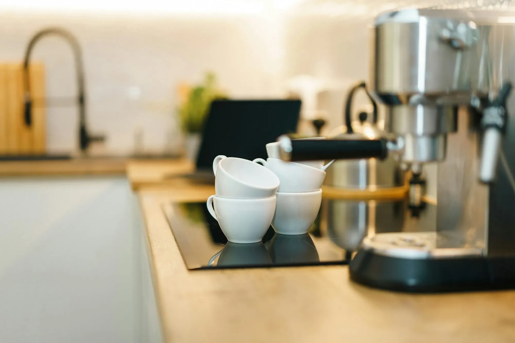 Espresso machine on a light kitchen counter with a stack of white cups beside it