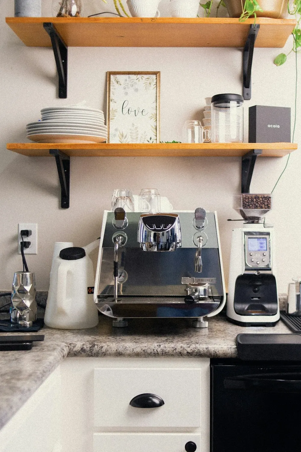 Espresso machine and grinder on a kitchen counter under wood floating shelves