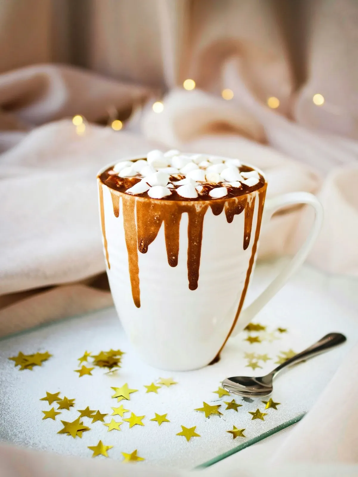 Mug of hot chocolate with caramel sauce dripping down the sides, topped with mini marshmallows