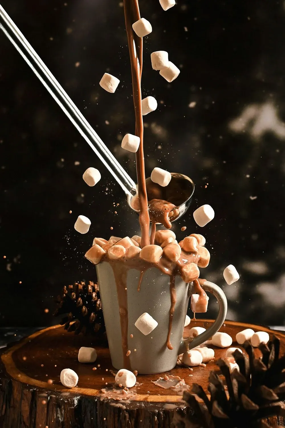 Mini marshmallows falling into a mug of hot chocolate on a dark rustic table