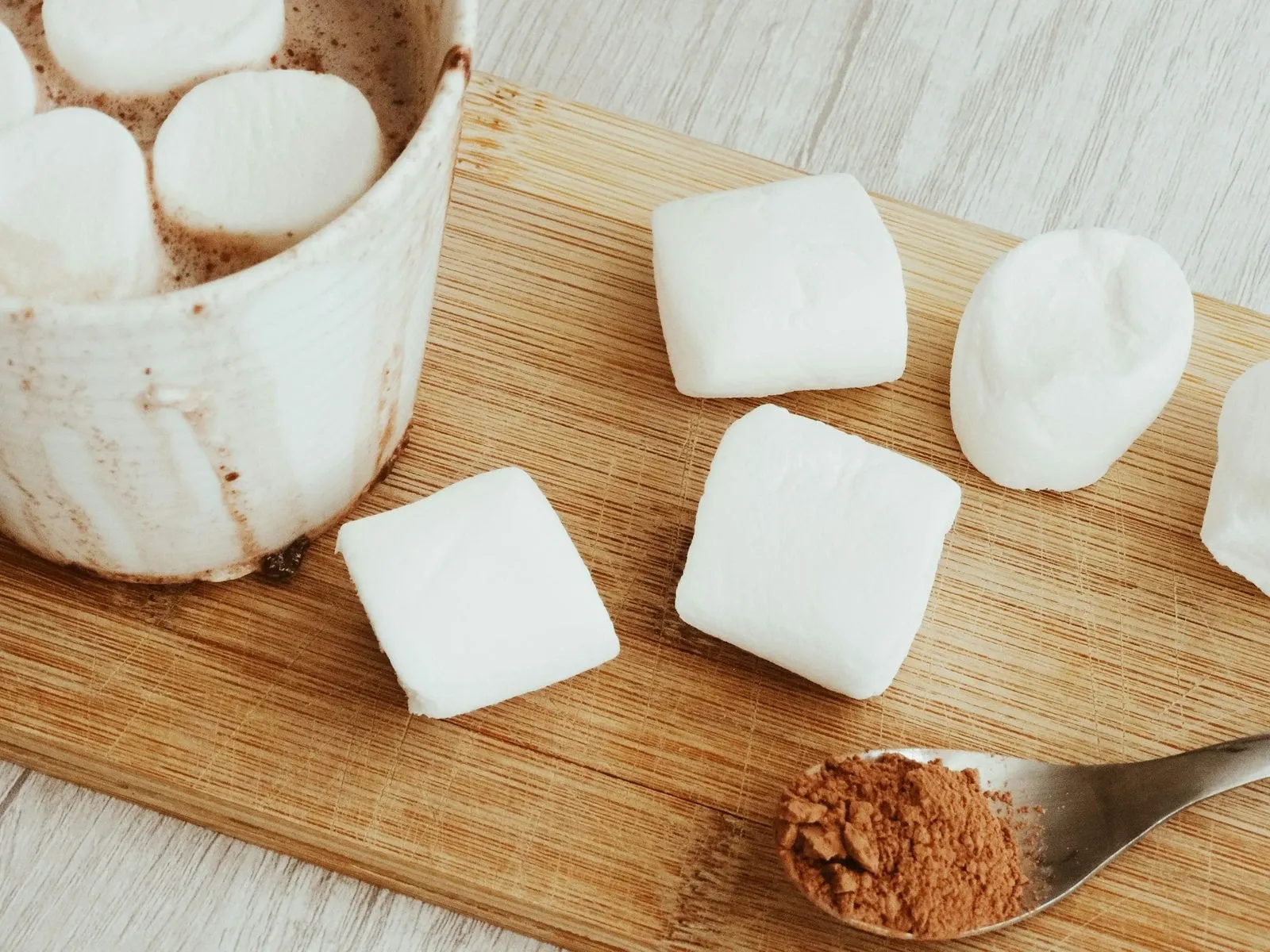 Wood board with large marshmallows, a mug of hot cocoa and a spoon of cocoa powder