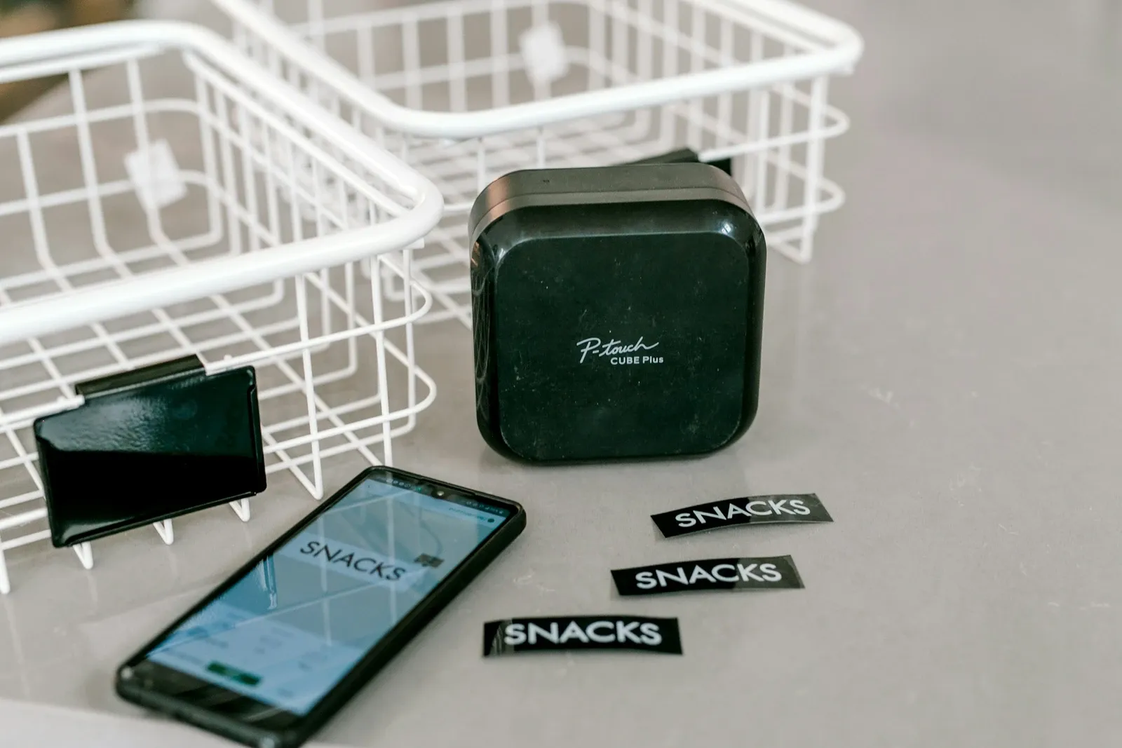 Label maker beside a smartphone app and printed black labels on a gray surface