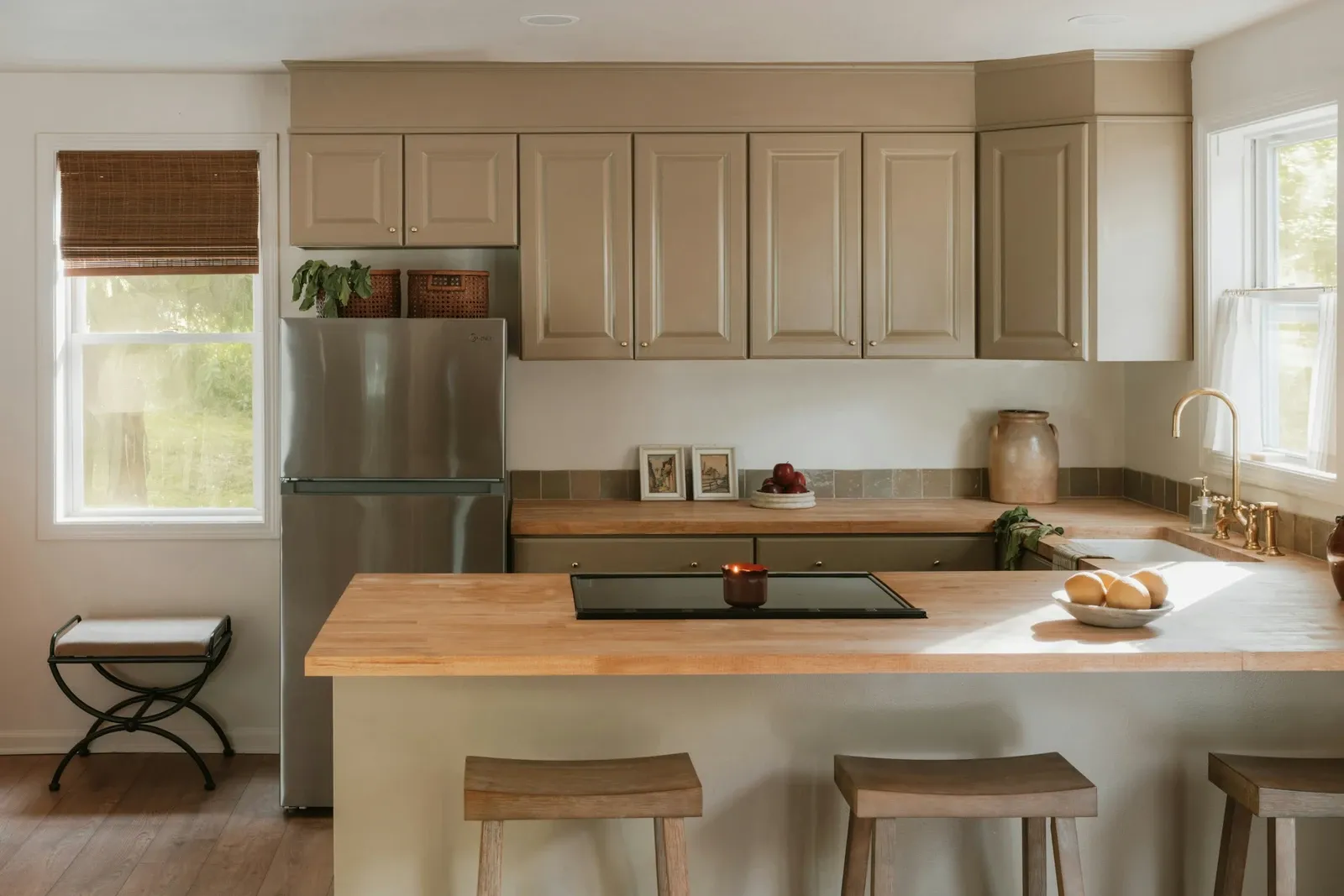 Bright modern kitchen with light wood countertops, a light wood island and pale cabinets under large windows