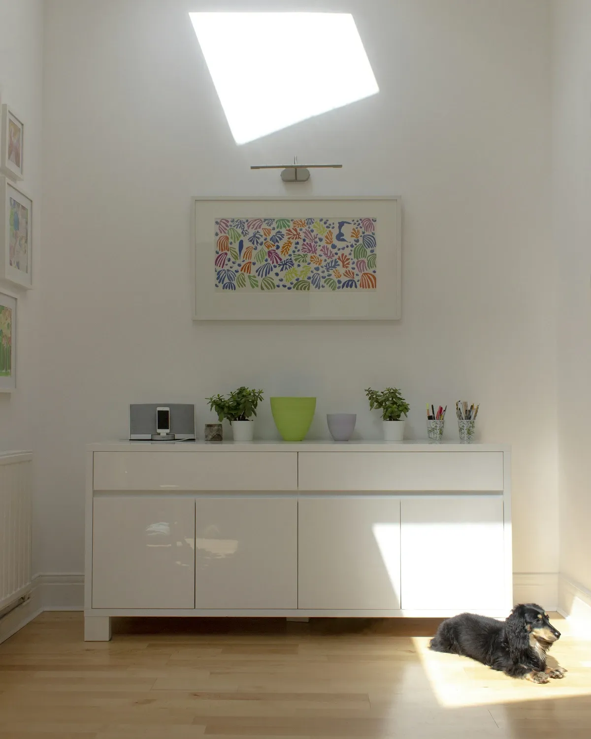 Low white sideboard with a few small objects on top in a bright room with a skylight and white walls