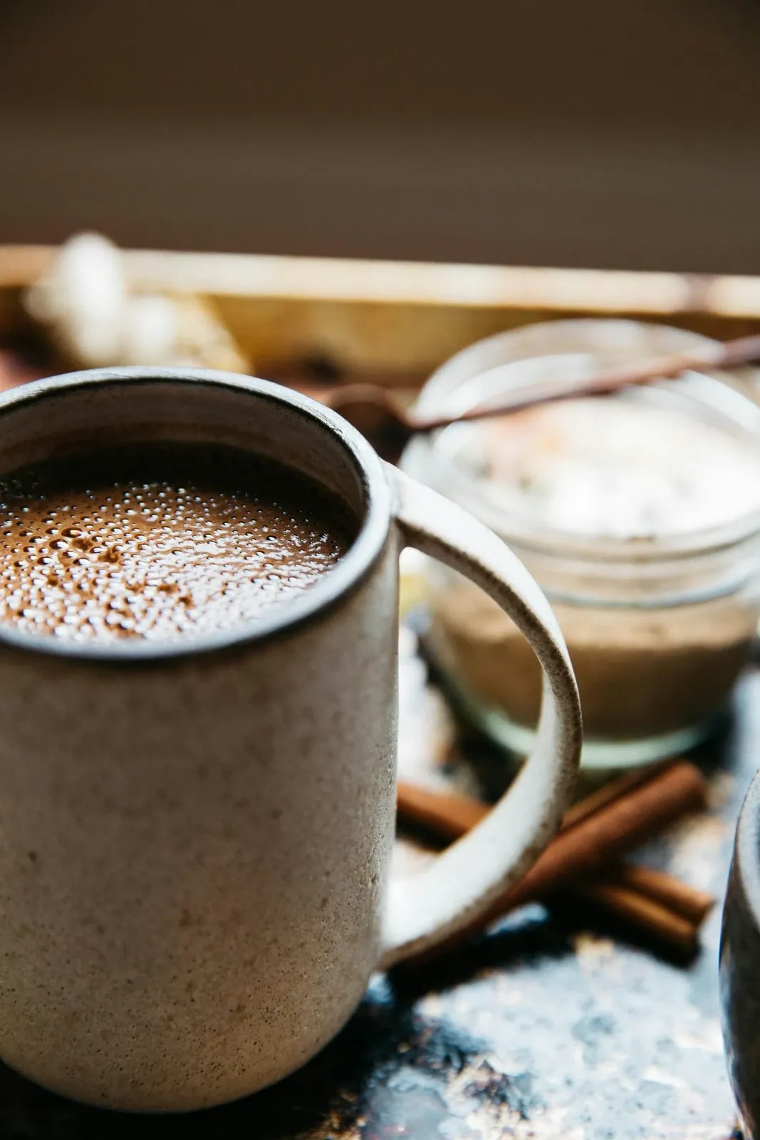 Stoneware mug of hot chocolate next to cinnamon sticks on a dark wood surface