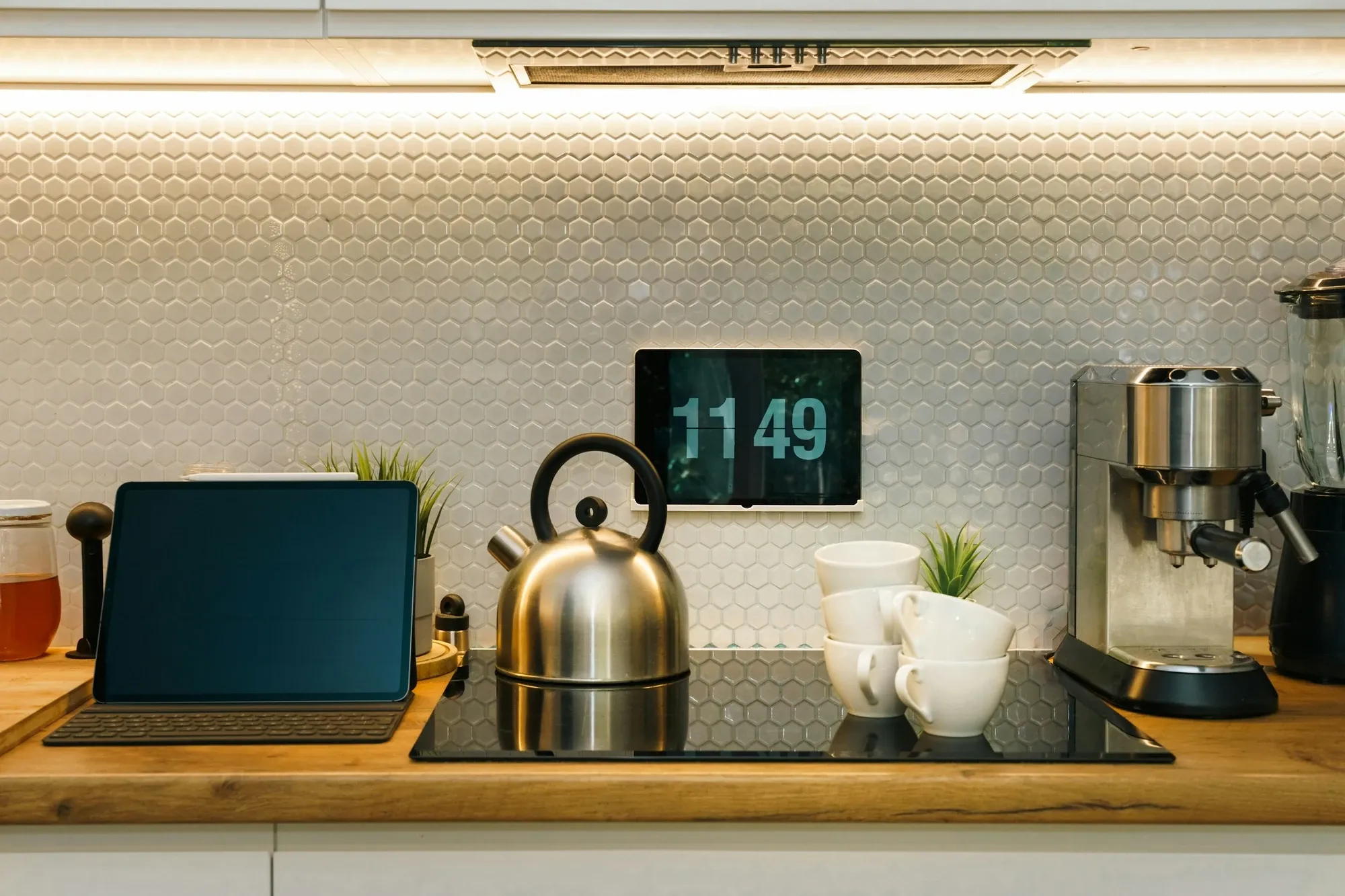 Modern kitchen counter with a kettle, a tablet and an espresso machine under a lit hexagon tile backsplash
