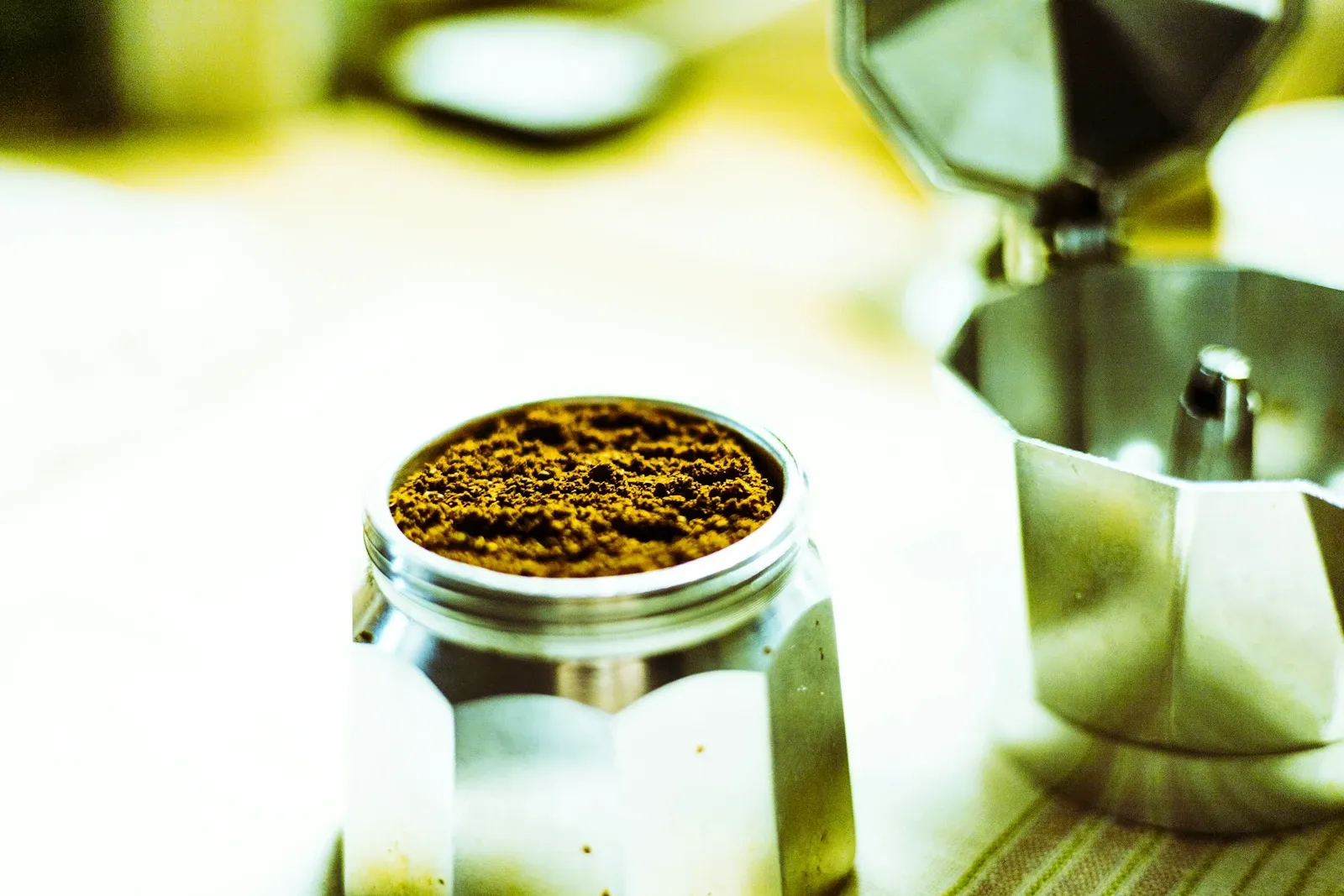 Filter basket of a moka pot filled level with ground coffee next to the upper chamber