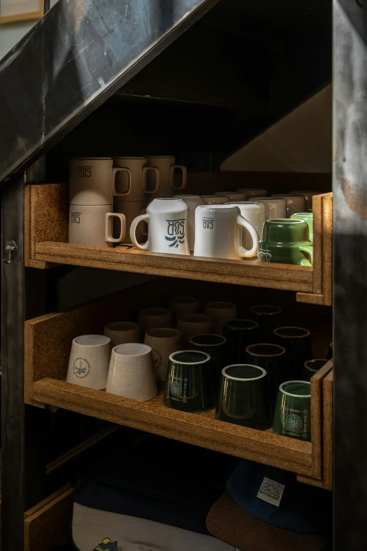 Wood cubby shelves under a staircase stacked with white and green mugs