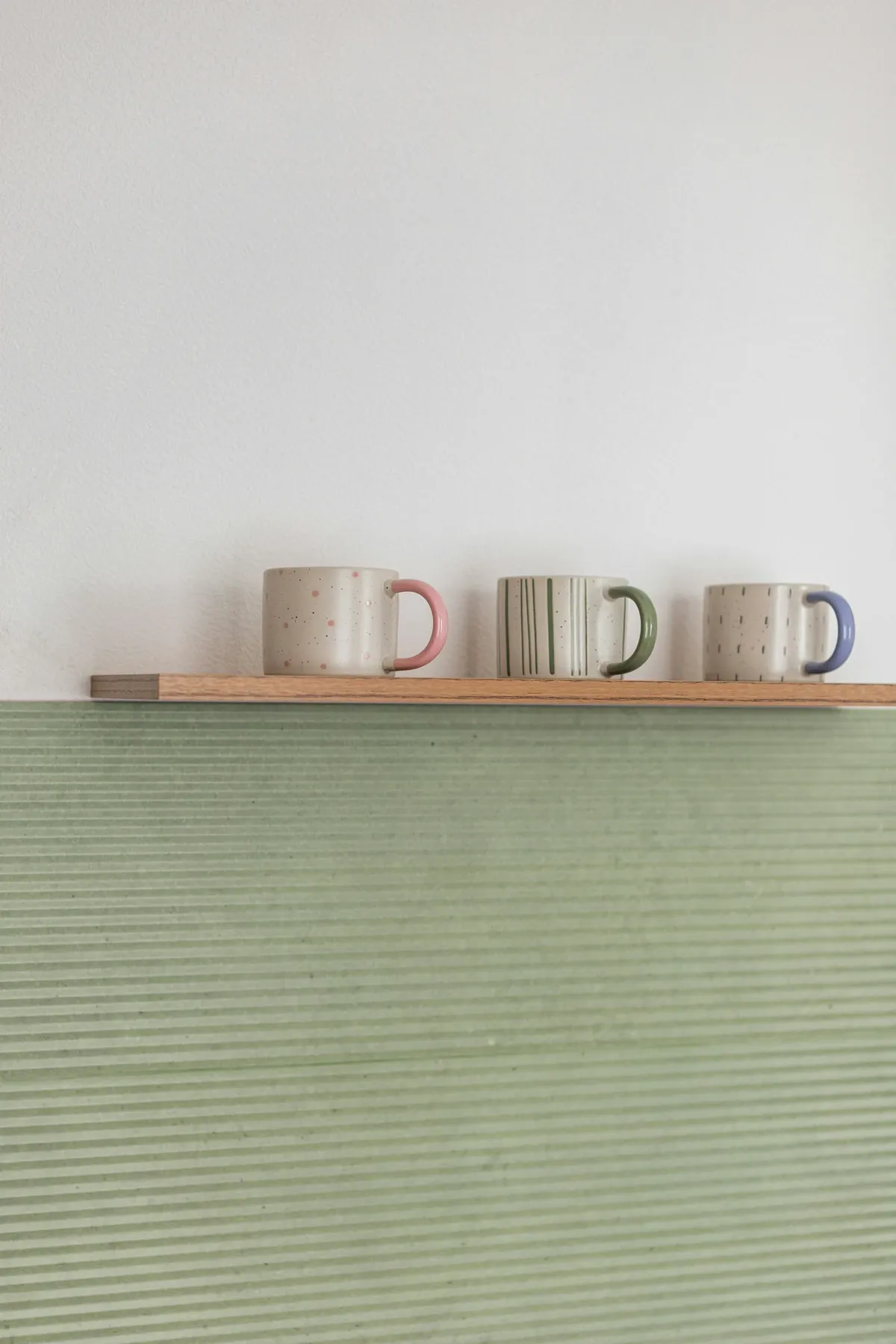 Narrow wood wall ledge holding three speckled mugs above a pale green wall panel