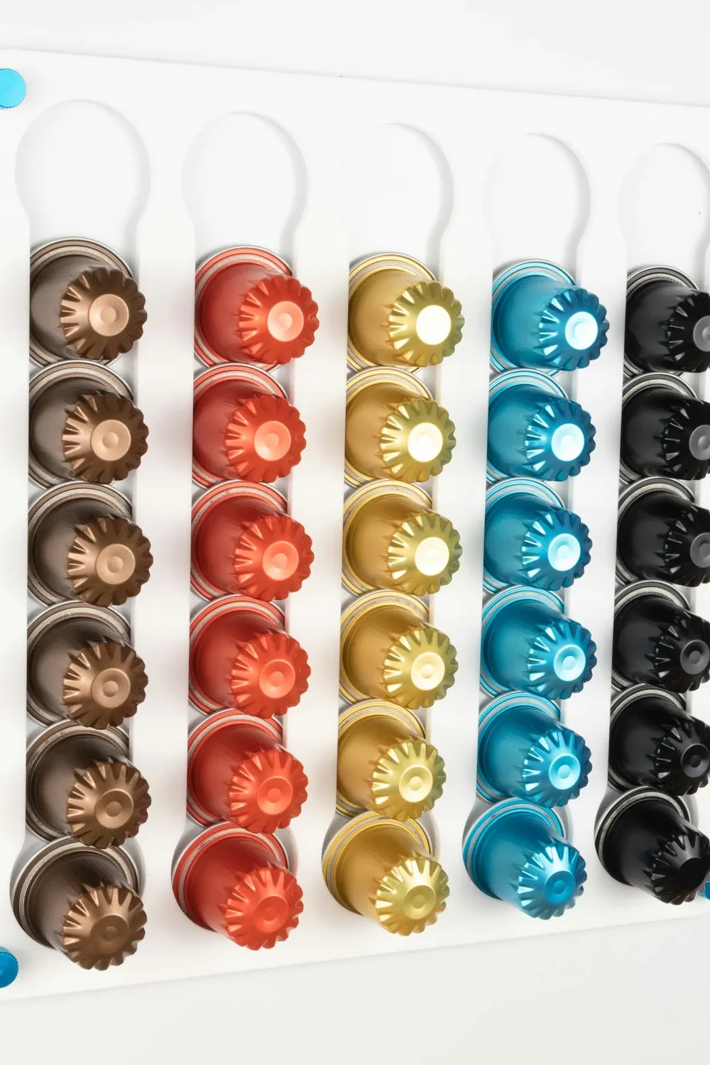 White wall-mounted capsule holder with six columns of colorful Nespresso pods