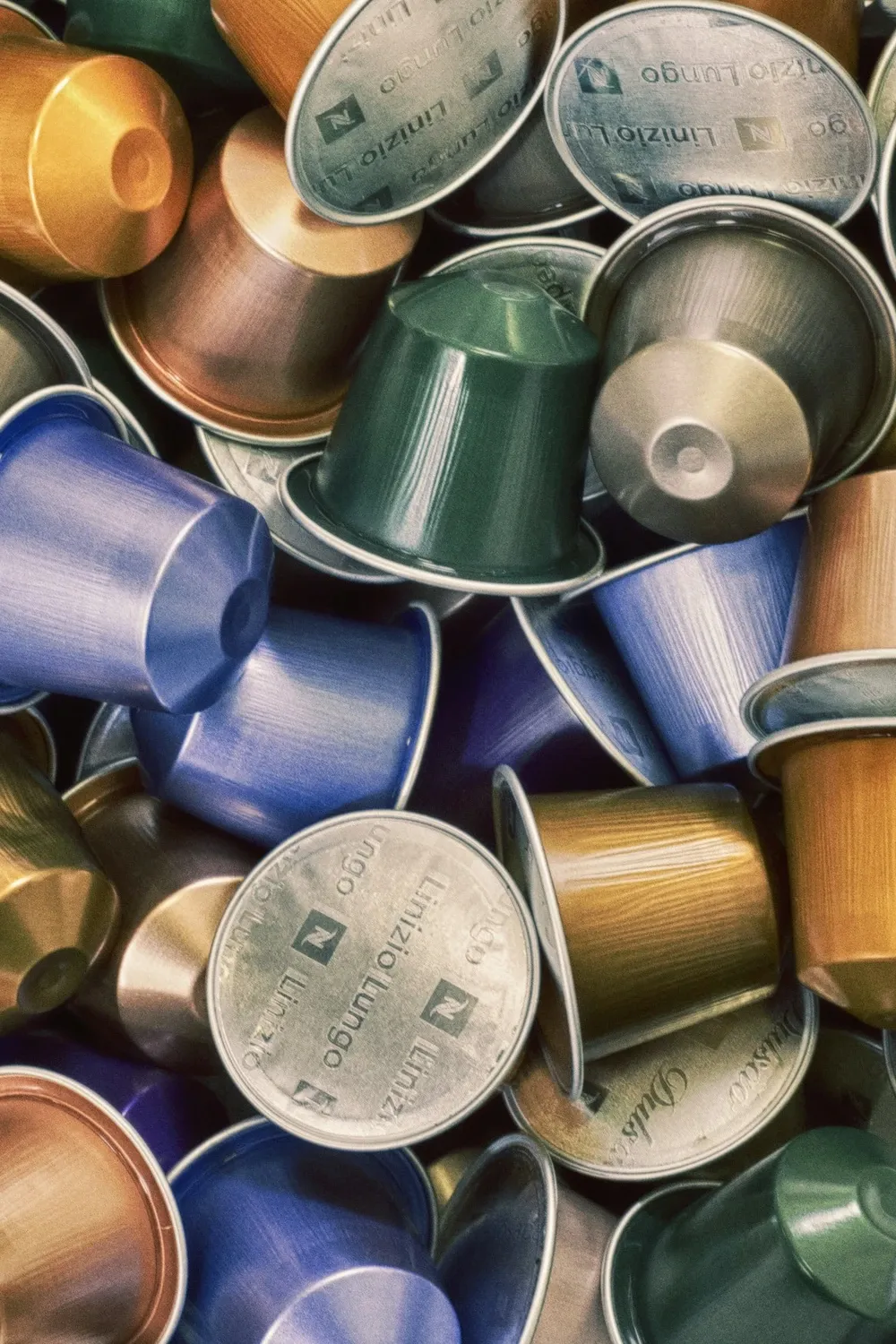 Pile of colorful aluminum Nespresso coffee capsules in gold, blue, green and silver