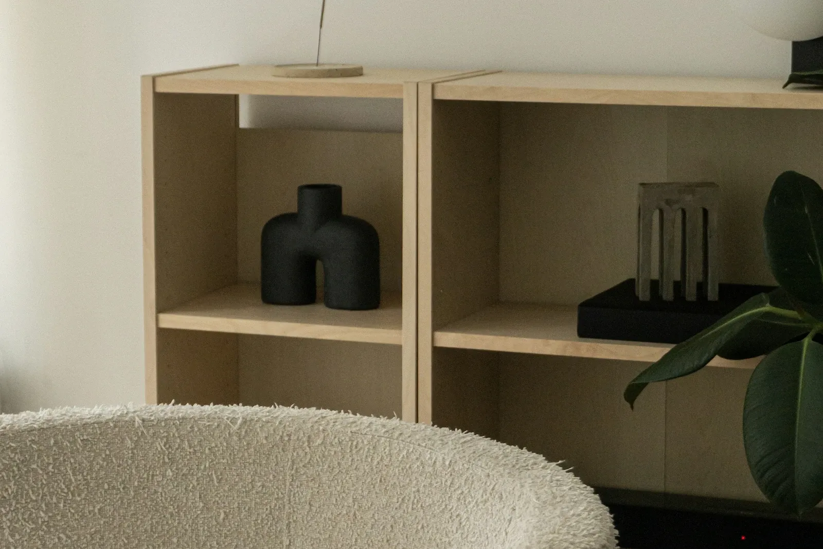 Open wood-tone cube shelving unit with a few decor pieces beside a cream boucle armchair in a living room