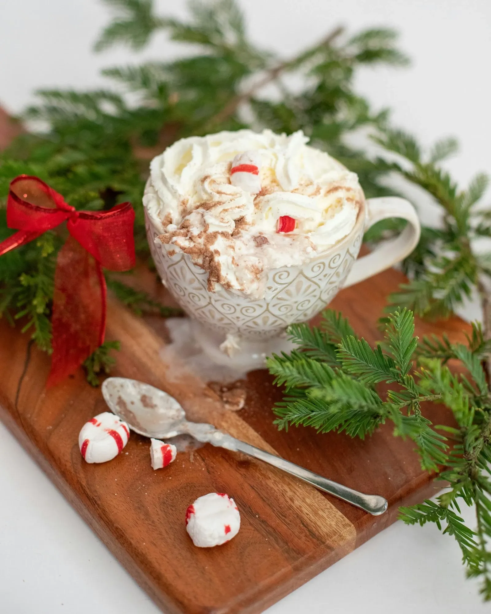 Glass mug of peppermint mocha with whipped cream and crushed peppermint candies on a wood board