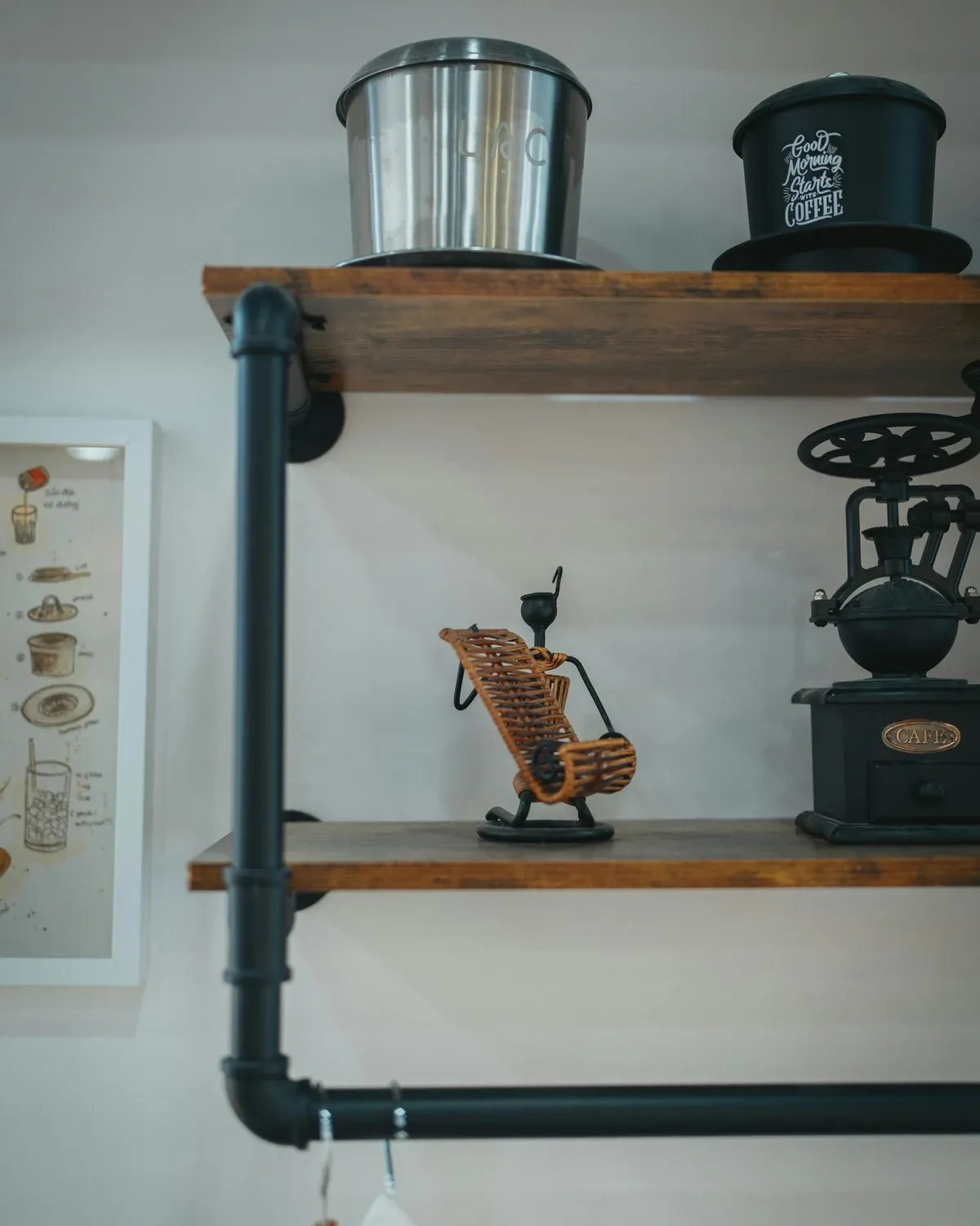 Black pipe brackets holding thick wood shelves with a coffee canister, a grinder and small decor above a white counter