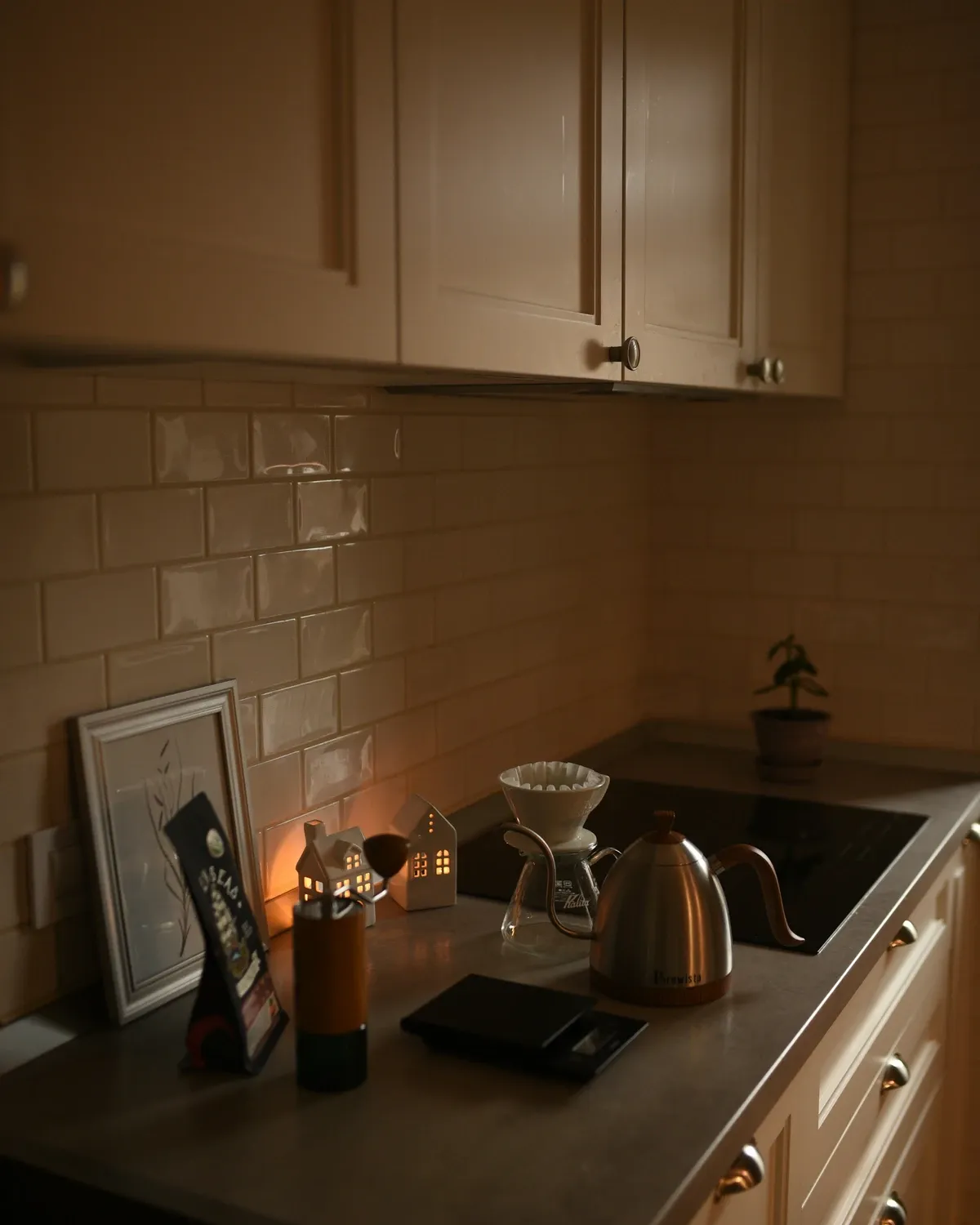 Kitchen counter with a pour-over dripper, a gooseneck kettle and a candle under cream shaker wall cabinets and a tile backsplash
