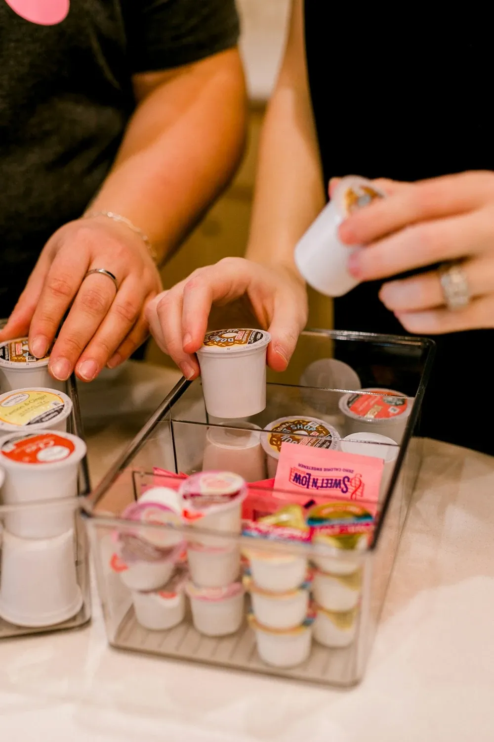 Hands picking single-serve pods from clear organizers filled with coffee and creamer cups