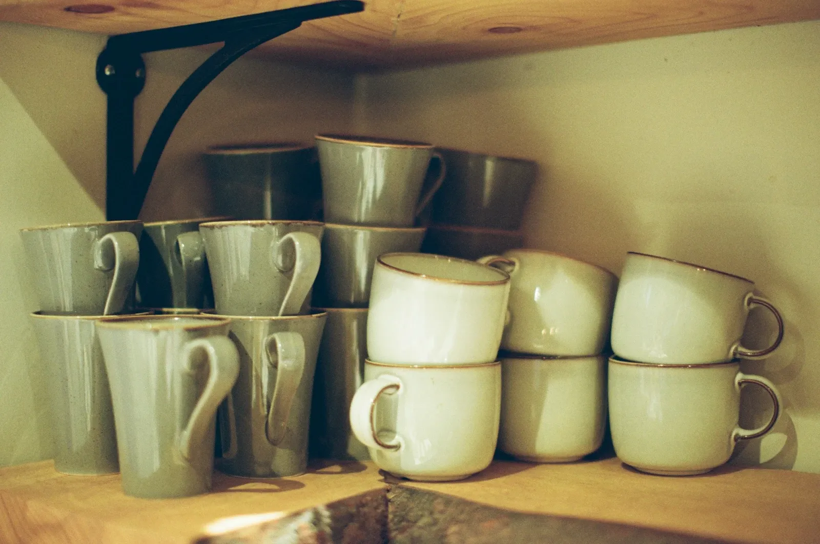 Sage and cream stoneware mugs stacked two high on a wooden shelf supported by a black iron bracket