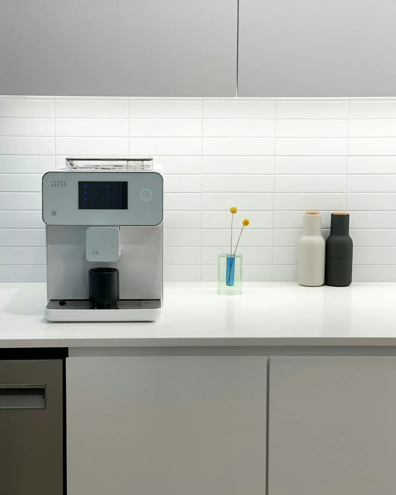 Automatic espresso machine on a white counter under gray upper cabinets with a white tile backsplash