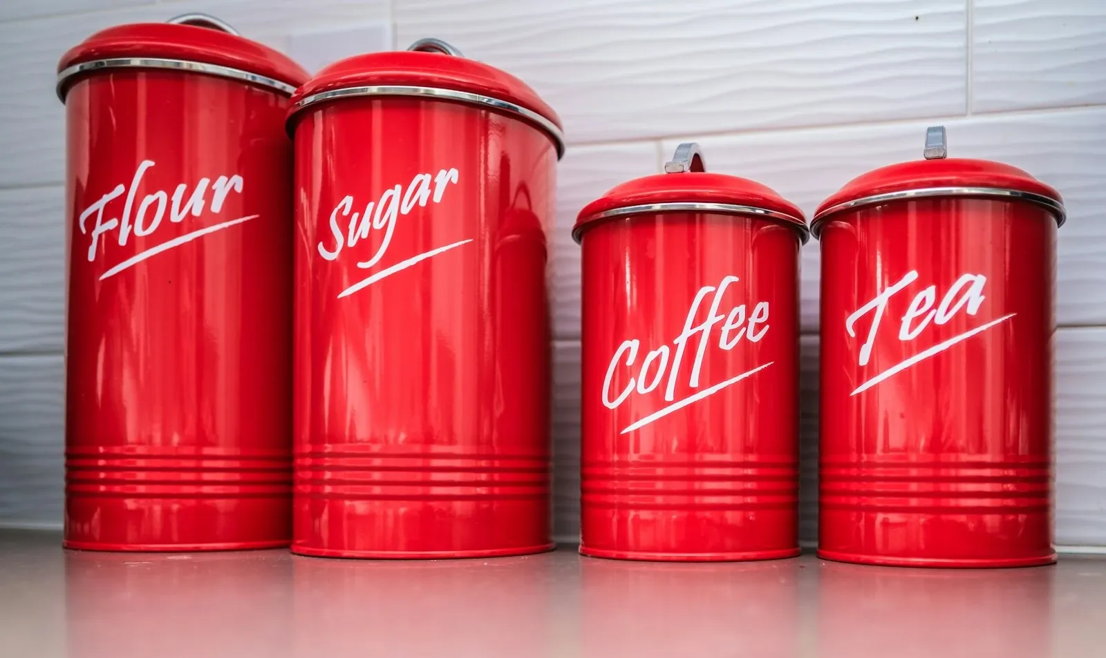 Two vintage red metal canisters labeled coffee and sugar on a wood surface