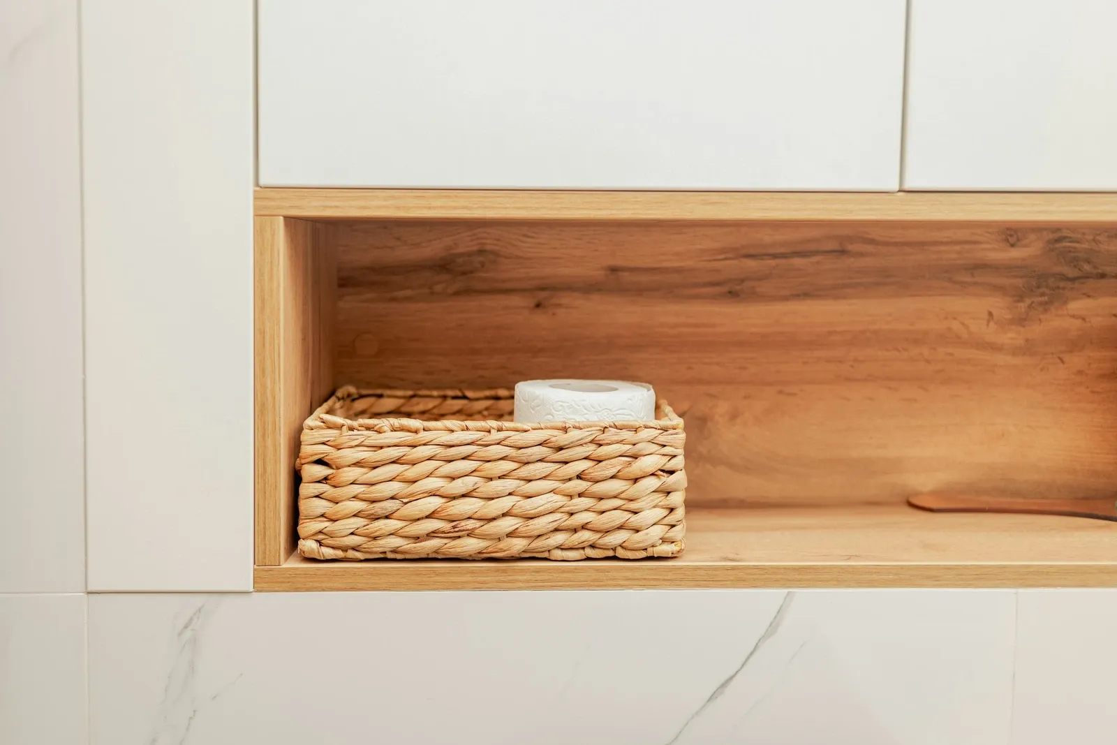 White wall cabinet with an open wood-lined niche holding a woven basket above a marble counter