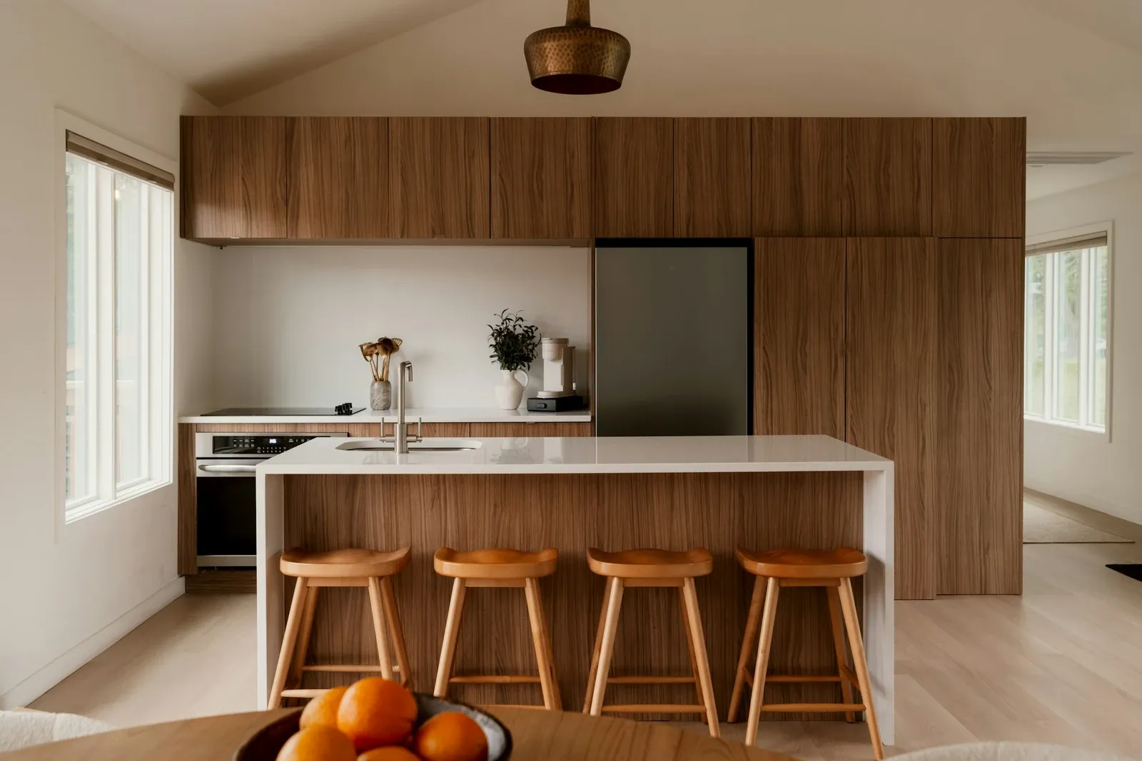 Modern kitchen with walnut cabinetry, a white island and four wooden stools under a pendant light