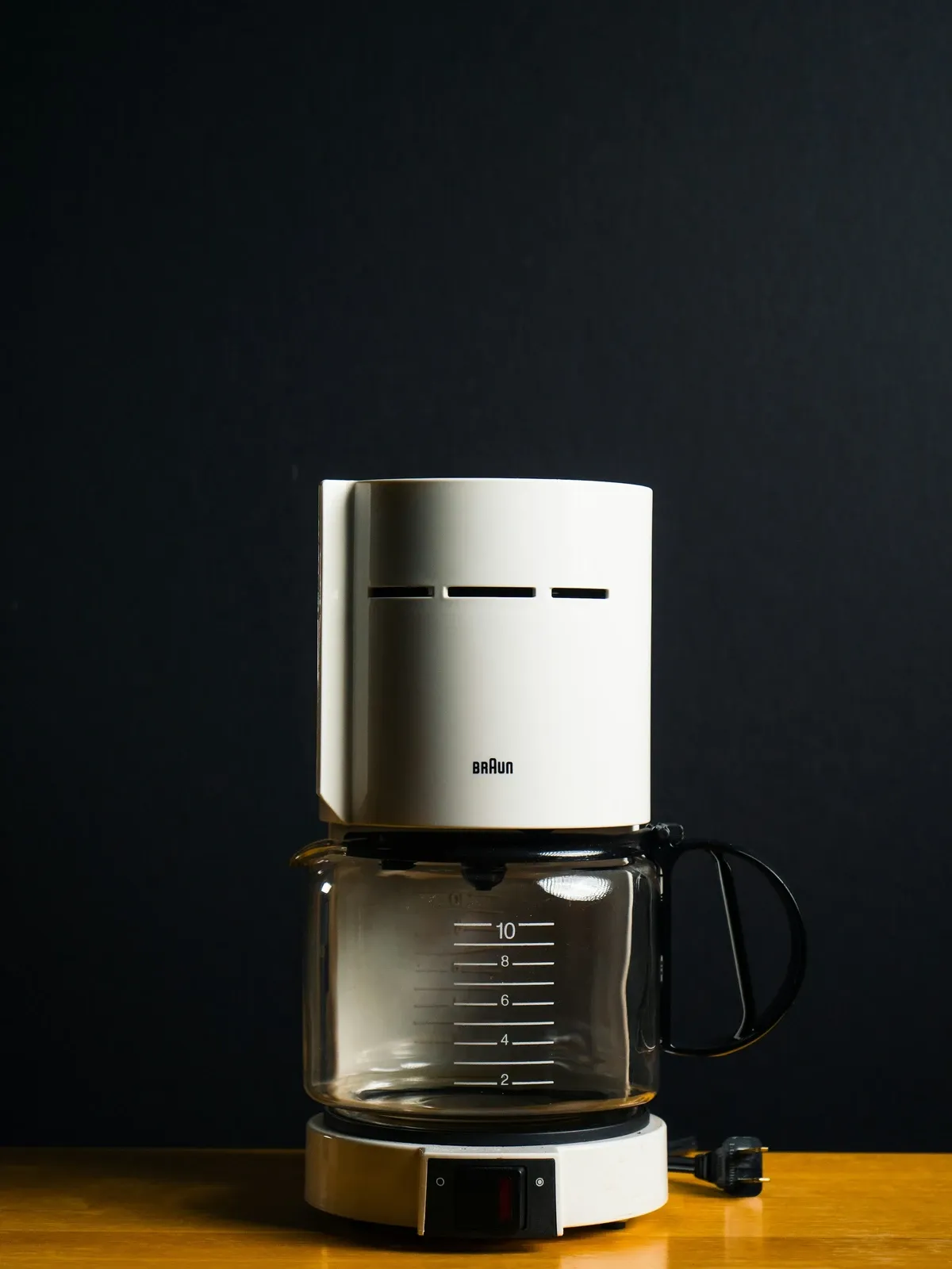 White drip coffee maker with a glass carafe on a wood counter against a dark wall